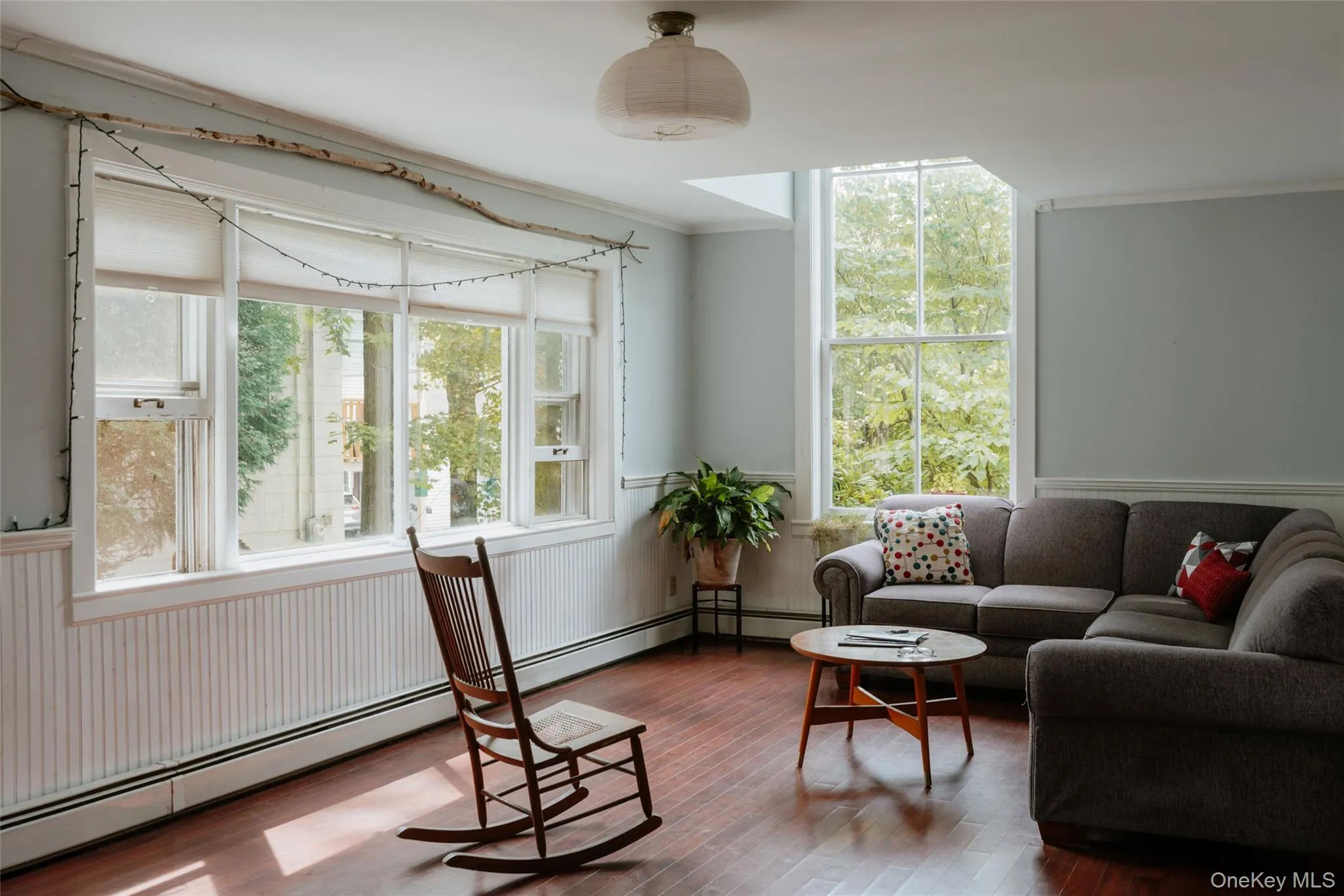 Living area with a baseboard radiator, ornamental molding, plenty of natural light, wood finished floors, and a wainscoted wall Living area with a baseboard radiator, ornamental molding, plenty of natural light, wood finished floors, and a wainscoted wall