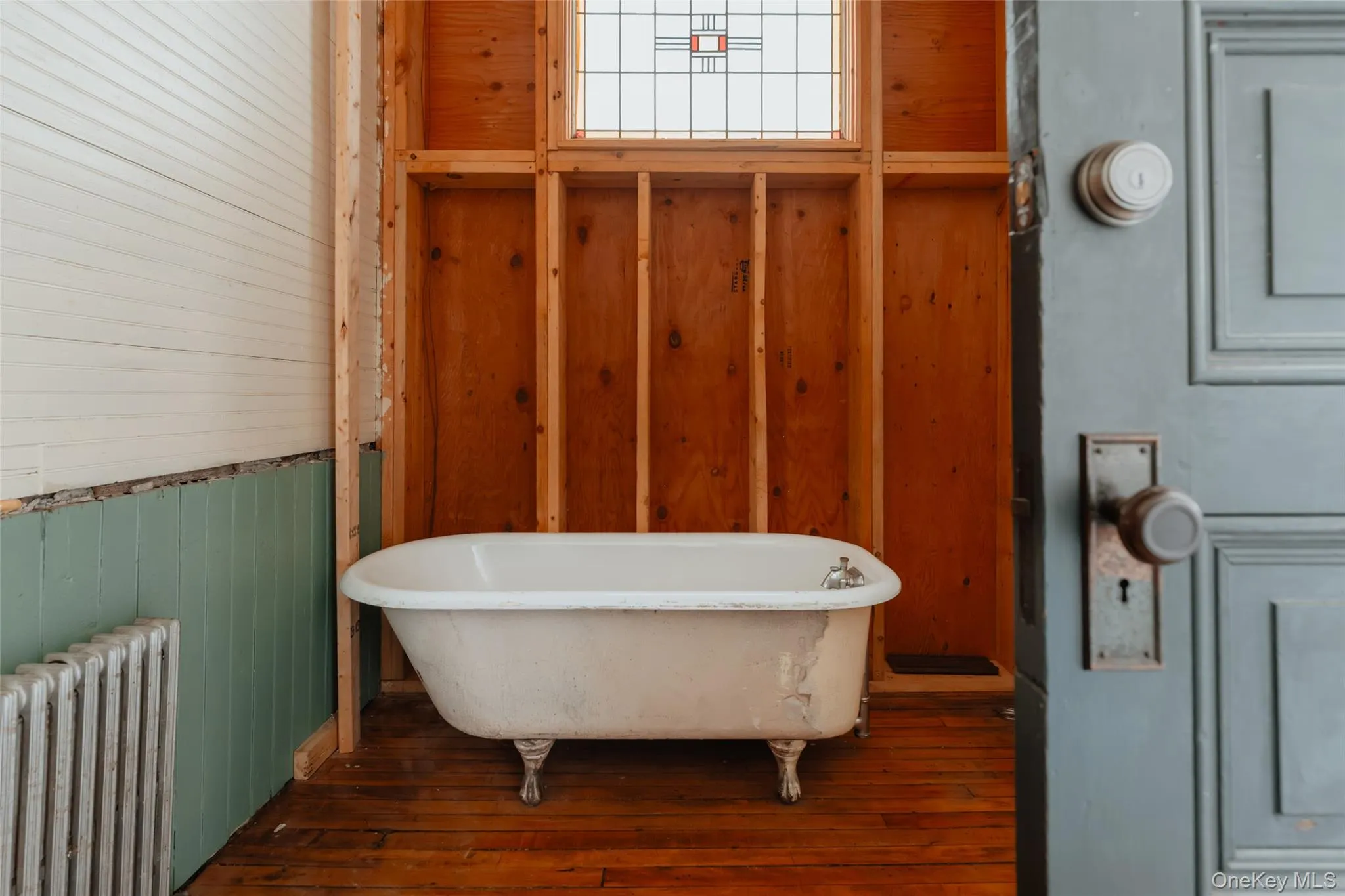 Full bath with wooden walls, radiator heating unit, a freestanding tub, and dark wood-style flooring Full bath with wooden walls, radiator heating unit, a freestanding tub, and dark wood-style flooring