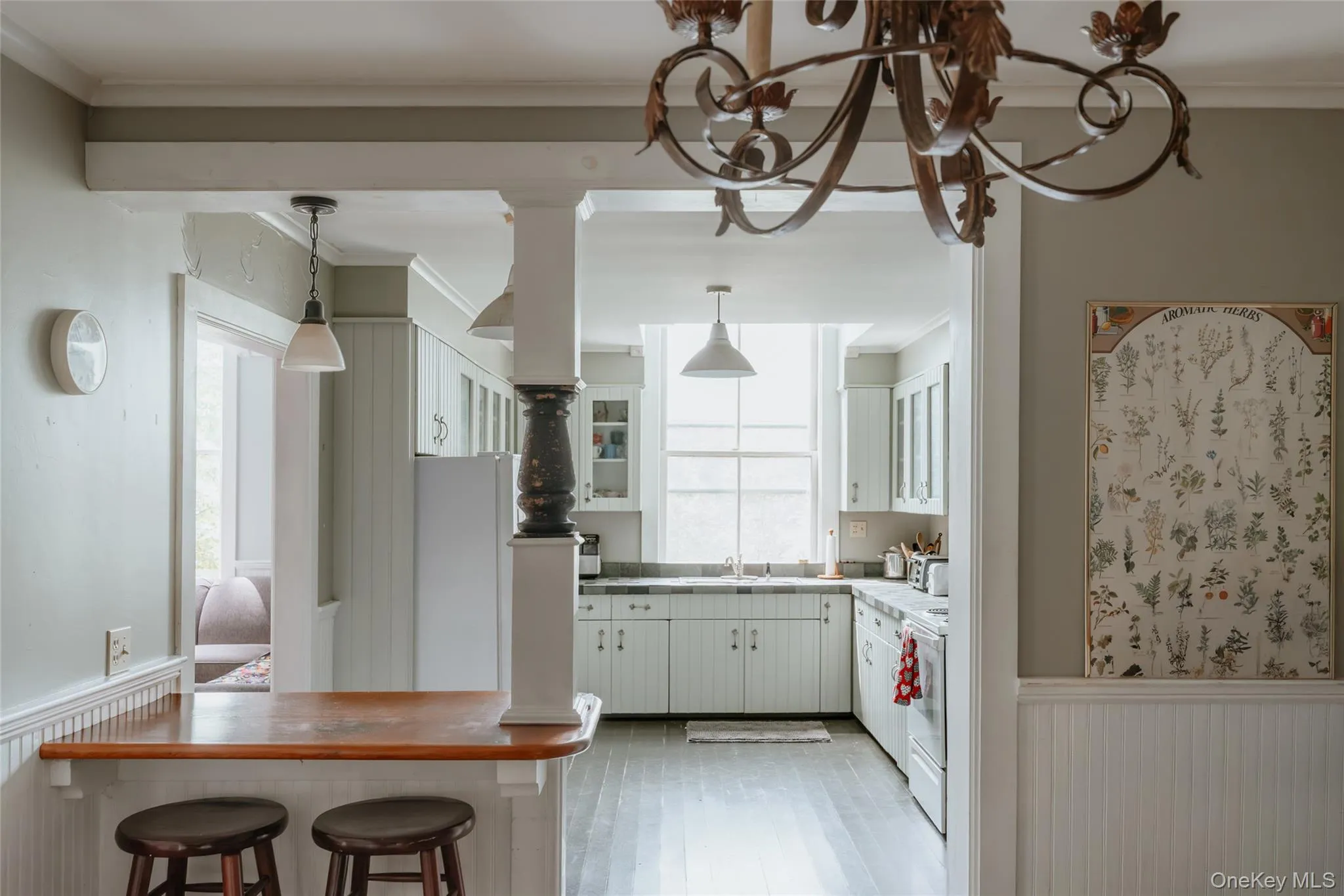 Kitchen with a wainscoted wall, ornamental molding, white cabinets, a kitchen bar, and hanging light fixtures Kitchen with a wainscoted wall, ornamental molding, white cabinets, a kitchen bar, and hanging light fixtures