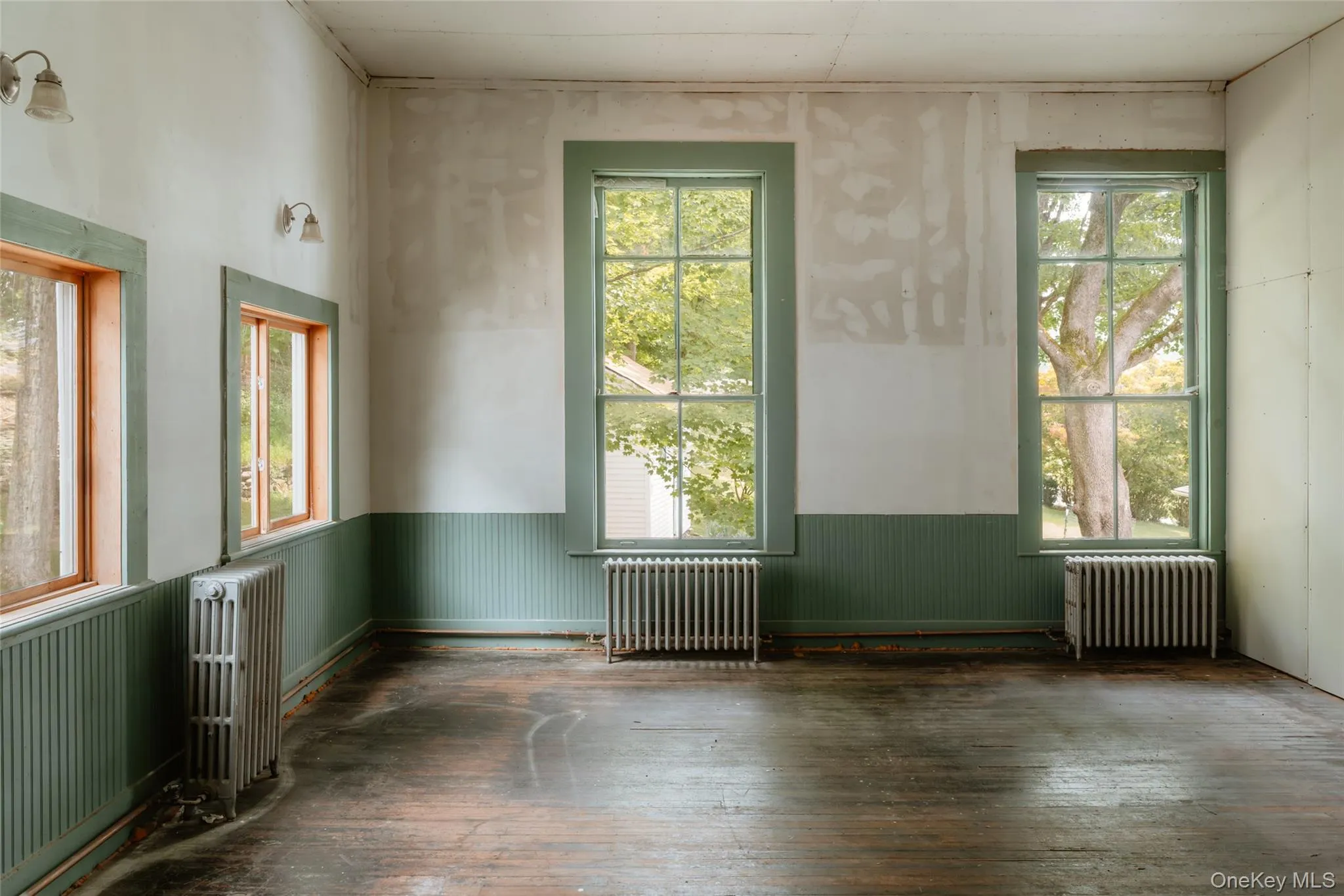 Empty room featuring radiator heating unit, wainscoting, and hardwood / wood-style flooring Empty room featuring radiator heating unit, wainscoting, and hardwood / wood-style flooring