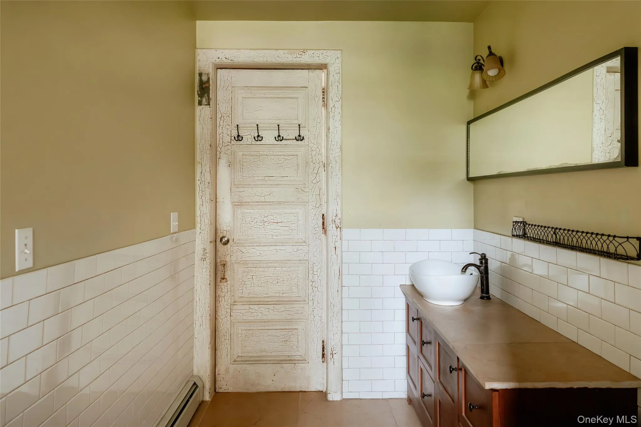 Bathroom with tile walls, tile patterned flooring, vanity, a baseboard heating unit, and a wainscoted wall Bathroom with tile walls, tile patterned flooring, vanity, a baseboard heating unit, and a wainscoted wall