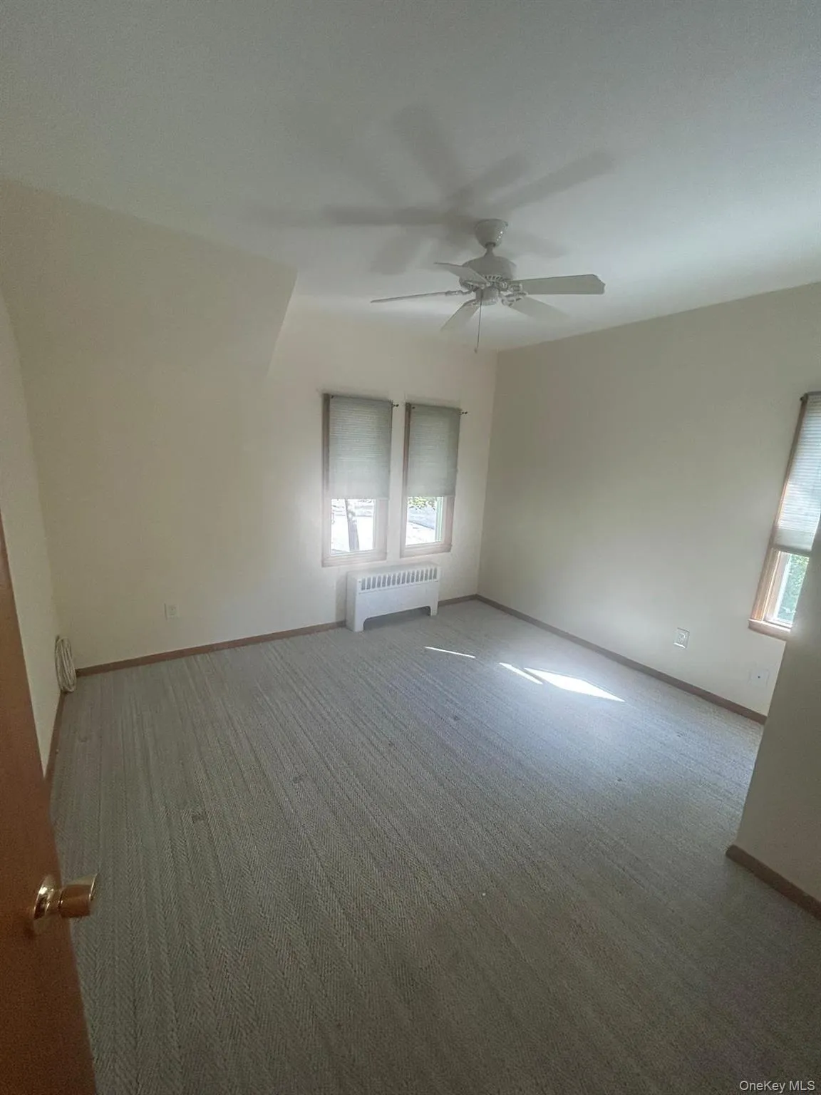 Empty room with radiator heating unit, carpet, and ceiling fan Empty room with radiator heating unit, carpet, and ceiling fan