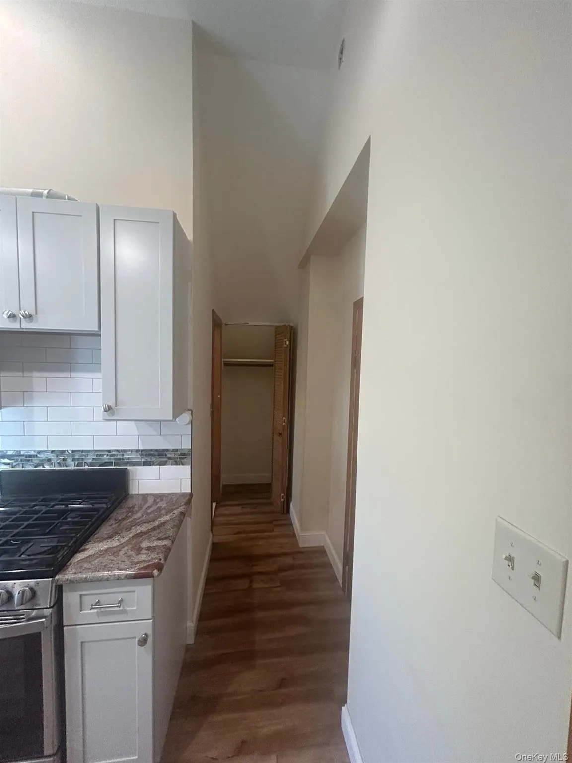 Kitchen featuring stainless steel gas range, light stone countertops, dark wood finished floors, backsplash, and a high ceiling Kitchen featuring stainless steel gas range, light stone countertops, dark wood finished floors, backsplash, and a high ceiling