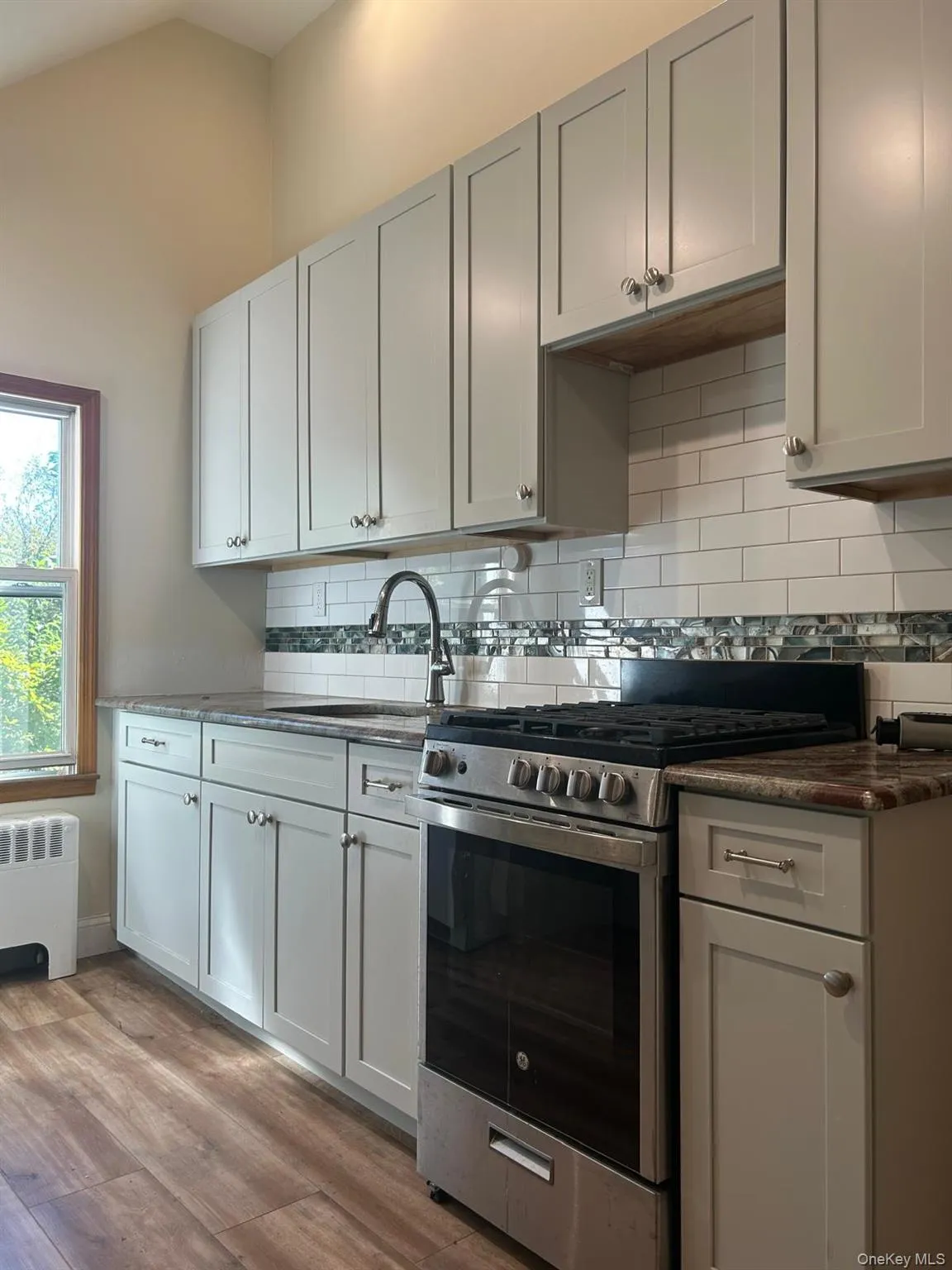Kitchen with gas range, radiator, light wood-style floors, dark stone countertops, and lofted ceiling Kitchen with gas range, radiator, light wood-style floors, dark stone countertops, and lofted ceiling