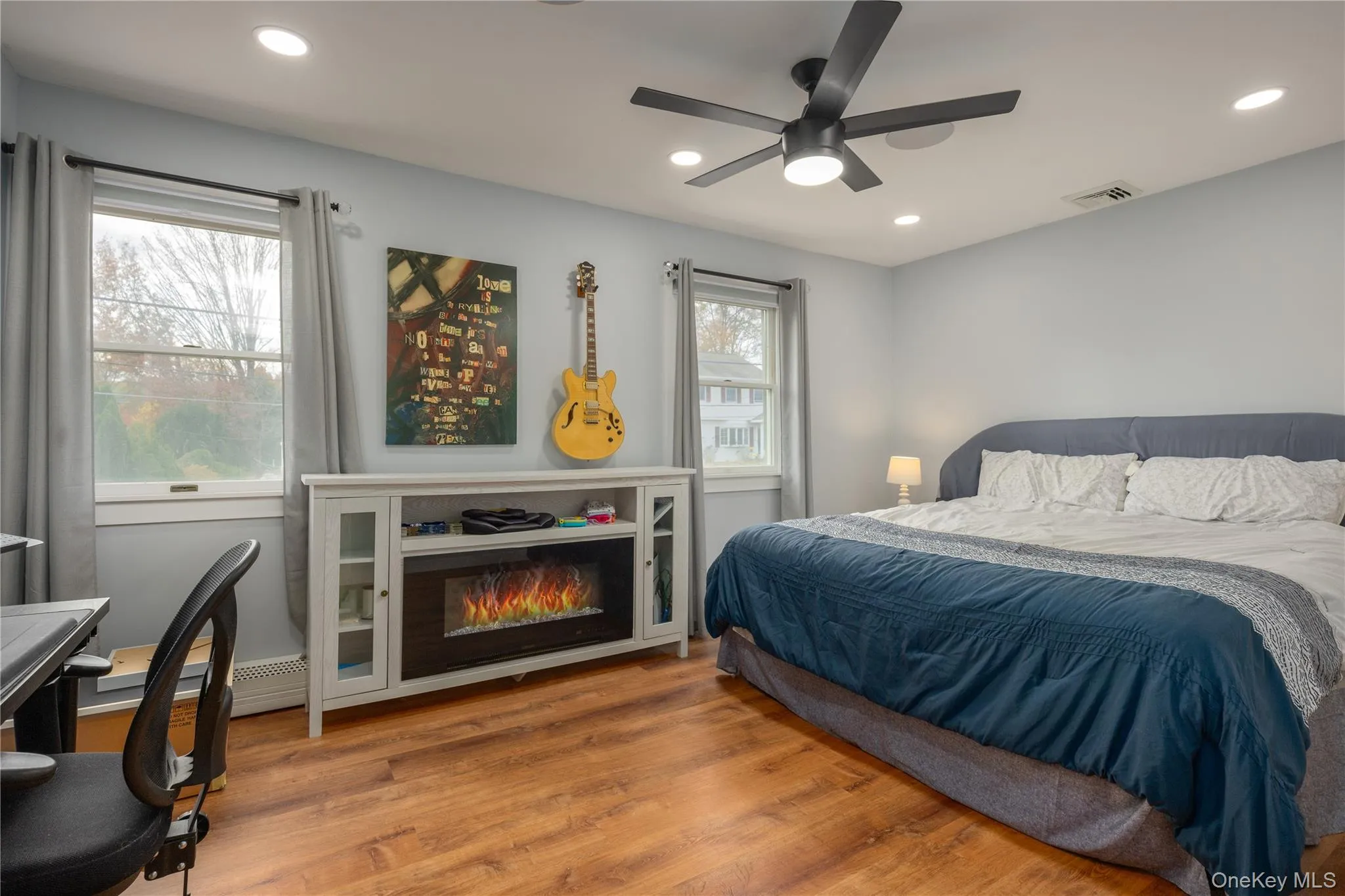 Bedroom with wood finished floors, recessed lighting, a ceiling fan, a glass covered fireplace, and a baseboard heating unit Bedroom with wood finished floors, recessed lighting, a ceiling fan, a glass covered fireplace, and a baseboard heating unit