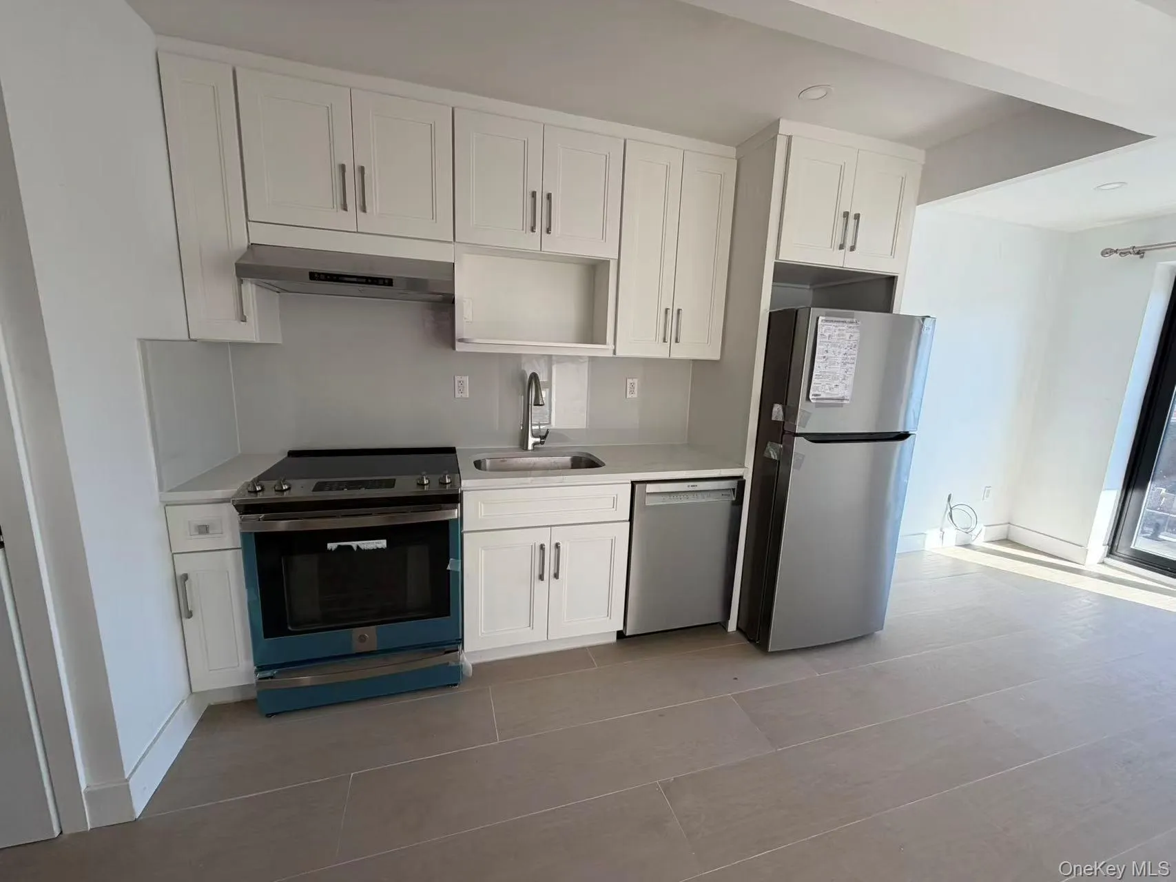 Kitchen with appliances with stainless steel finishes, white cabinetry, under cabinet range hood, and tile patterned floors Kitchen with appliances with stainless steel finishes, white cabinetry, under cabinet range hood, and tile patterned floors