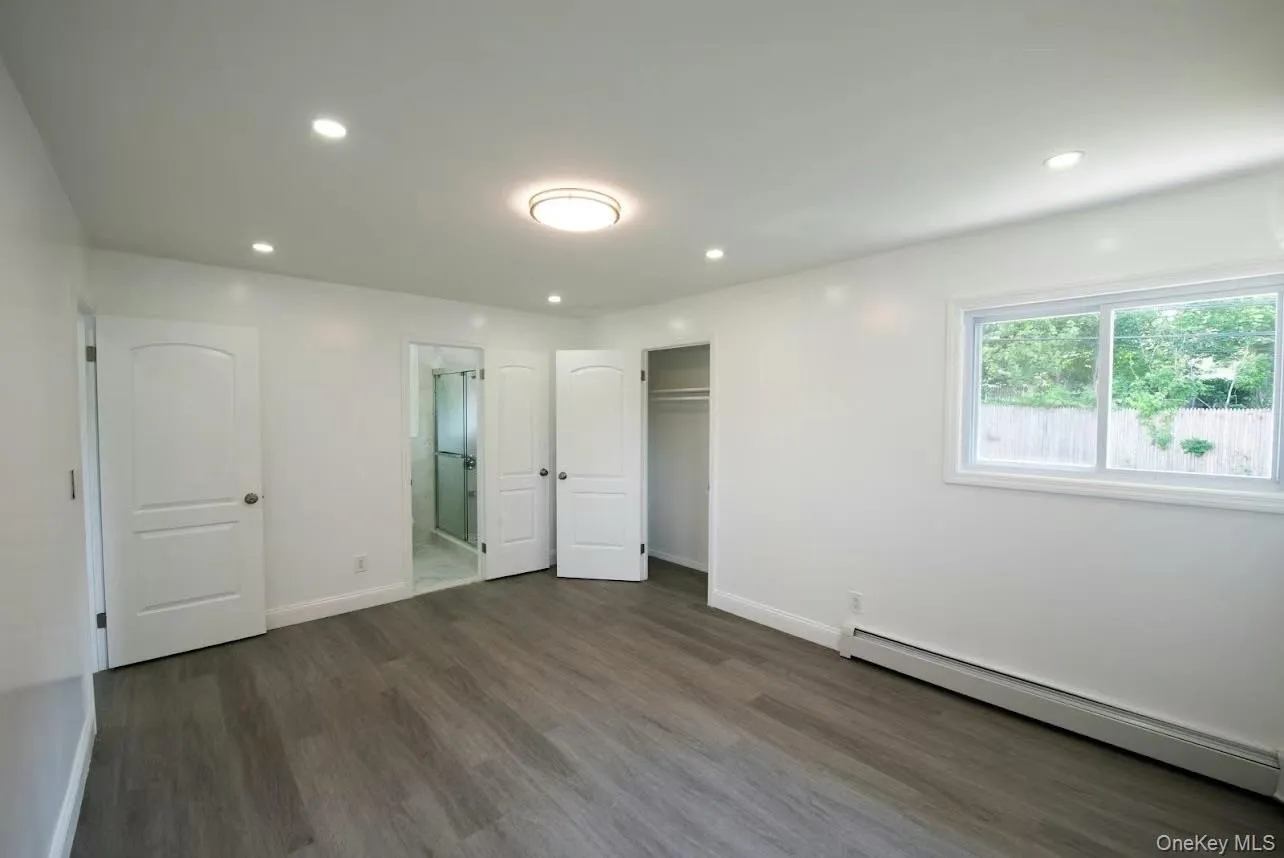 Unfurnished bedroom with a baseboard radiator, dark wood-style flooring, recessed lighting, ensuite bathroom, and a closet Unfurnished bedroom with a baseboard radiator, dark wood-style flooring, recessed lighting, ensuite bathroom, and a closet
