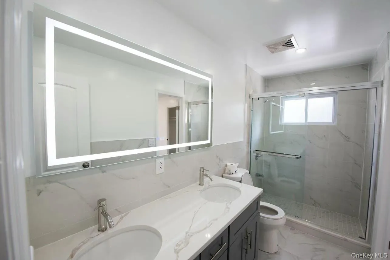 Bathroom with tile walls, double vanity, a marble finish shower, light marble finish floors, and a wainscoted wall Bathroom with tile walls, double vanity, a marble finish shower, light marble finish floors, and a wainscoted wall