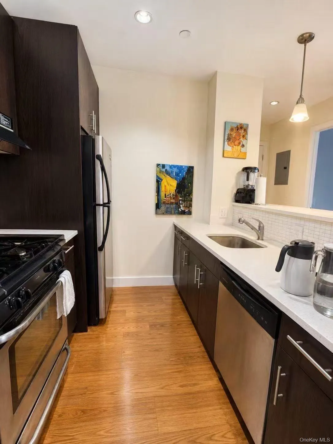 Kitchen featuring dark brown cabinetry, stainless steel appliances, decorative light fixtures, light wood finished floors, and recessed lighting Kitchen featuring dark brown cabinetry, stainless steel appliances, decorative light fixtures, light wood finished floors, and recessed lighting