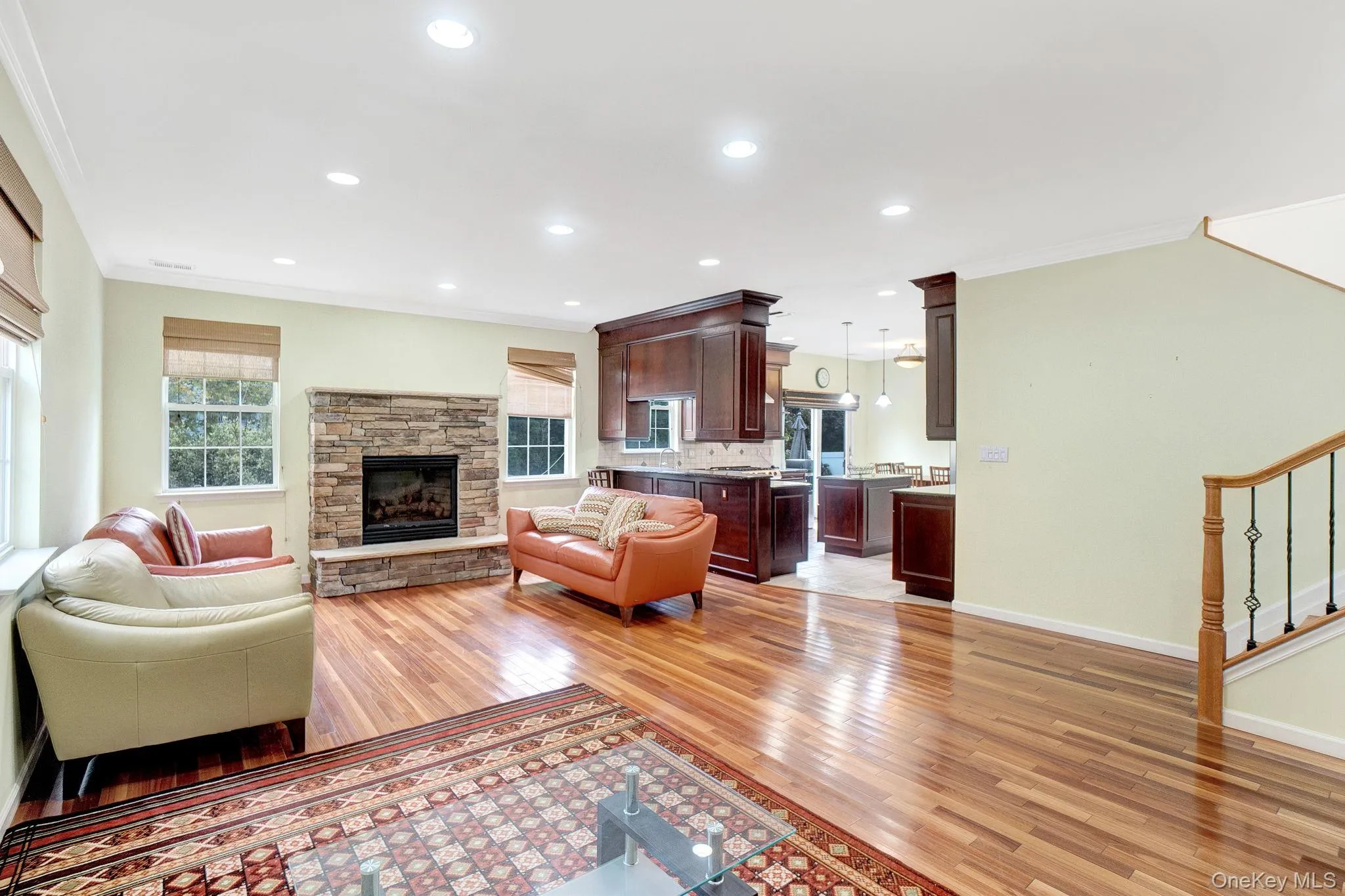 Living room with crown molding, light wood finished floors, recessed lighting, stairway, and a stone fireplace Living room with crown molding, light wood finished floors, recessed lighting, stairway, and a stone fireplace