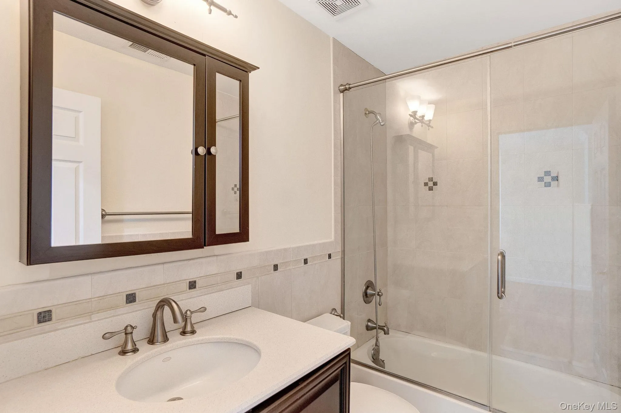 Bathroom with combined bath / shower with glass door, vanity, and tile walls Bathroom with combined bath / shower with glass door, vanity, and tile walls