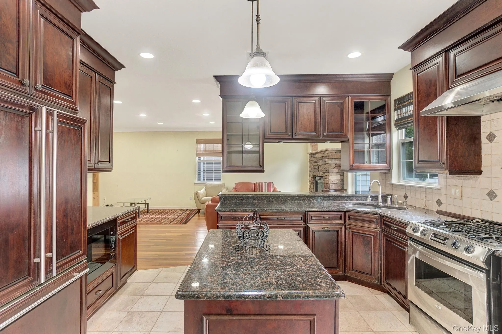 Kitchen featuring built in appliances, glass insert cabinets, dark stone counters, pendant lighting, and backsplash Kitchen featuring built in appliances, glass insert cabinets, dark stone counters, pendant lighting, and backsplash