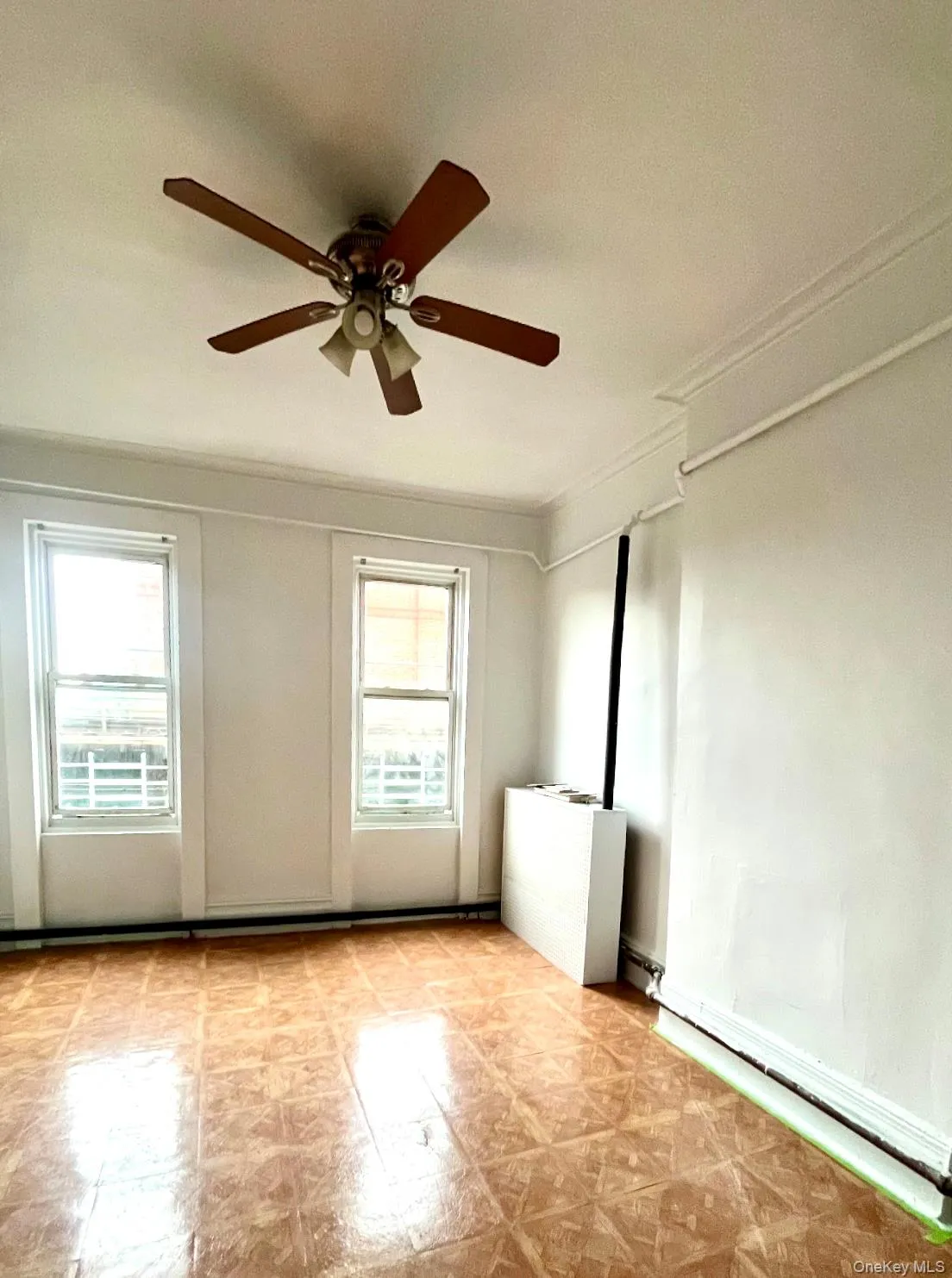 Empty room with a ceiling fan, ornamental molding, light flooring, and baseboard heating Empty room with a ceiling fan, ornamental molding, light flooring, and baseboard heating