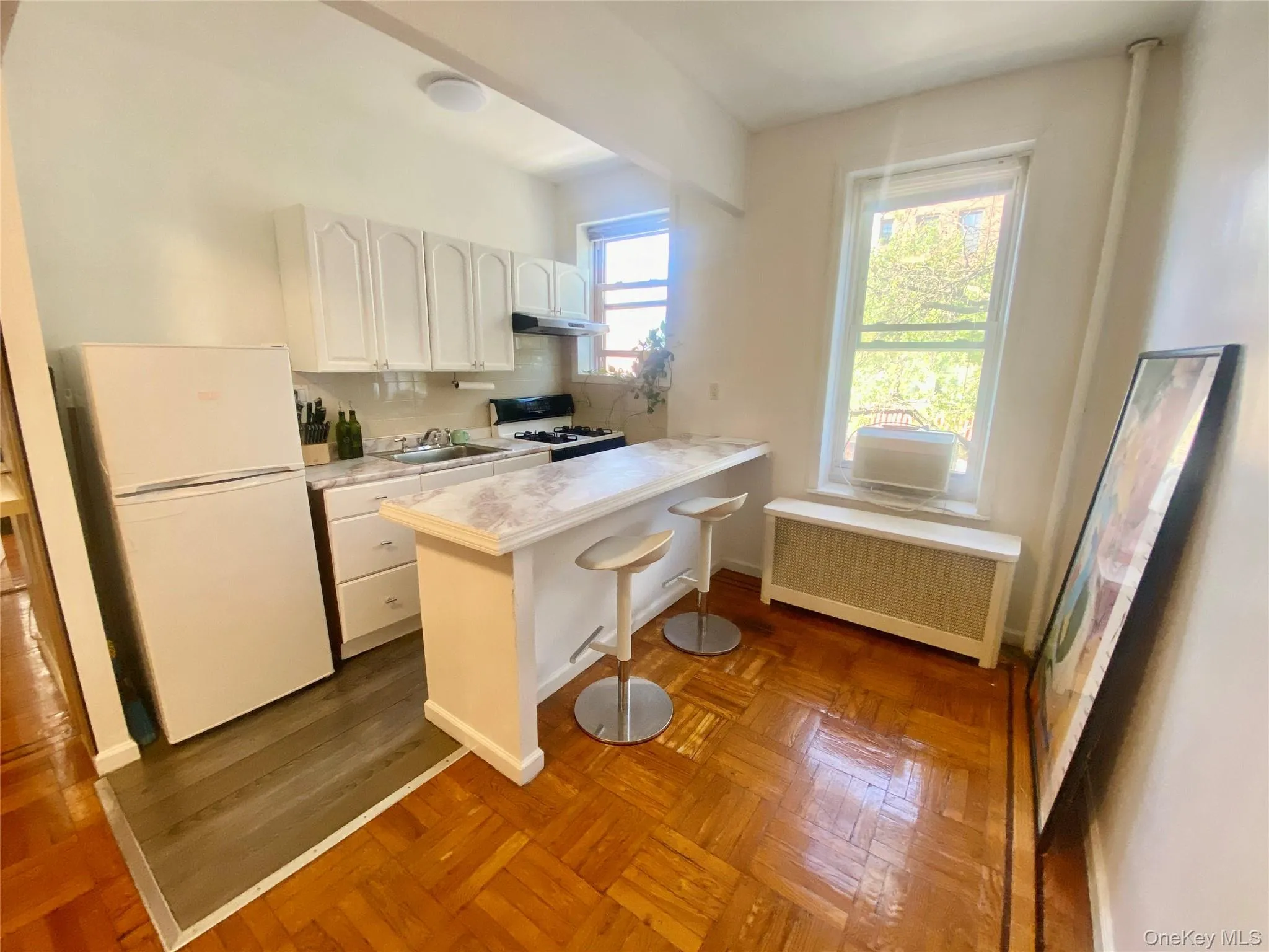 Kitchen with a kitchen bar, freestanding refrigerator, white cabinetry, radiator heating unit, and gas range oven Kitchen with a kitchen bar, freestanding refrigerator, white cabinetry, radiator heating unit, and gas range oven