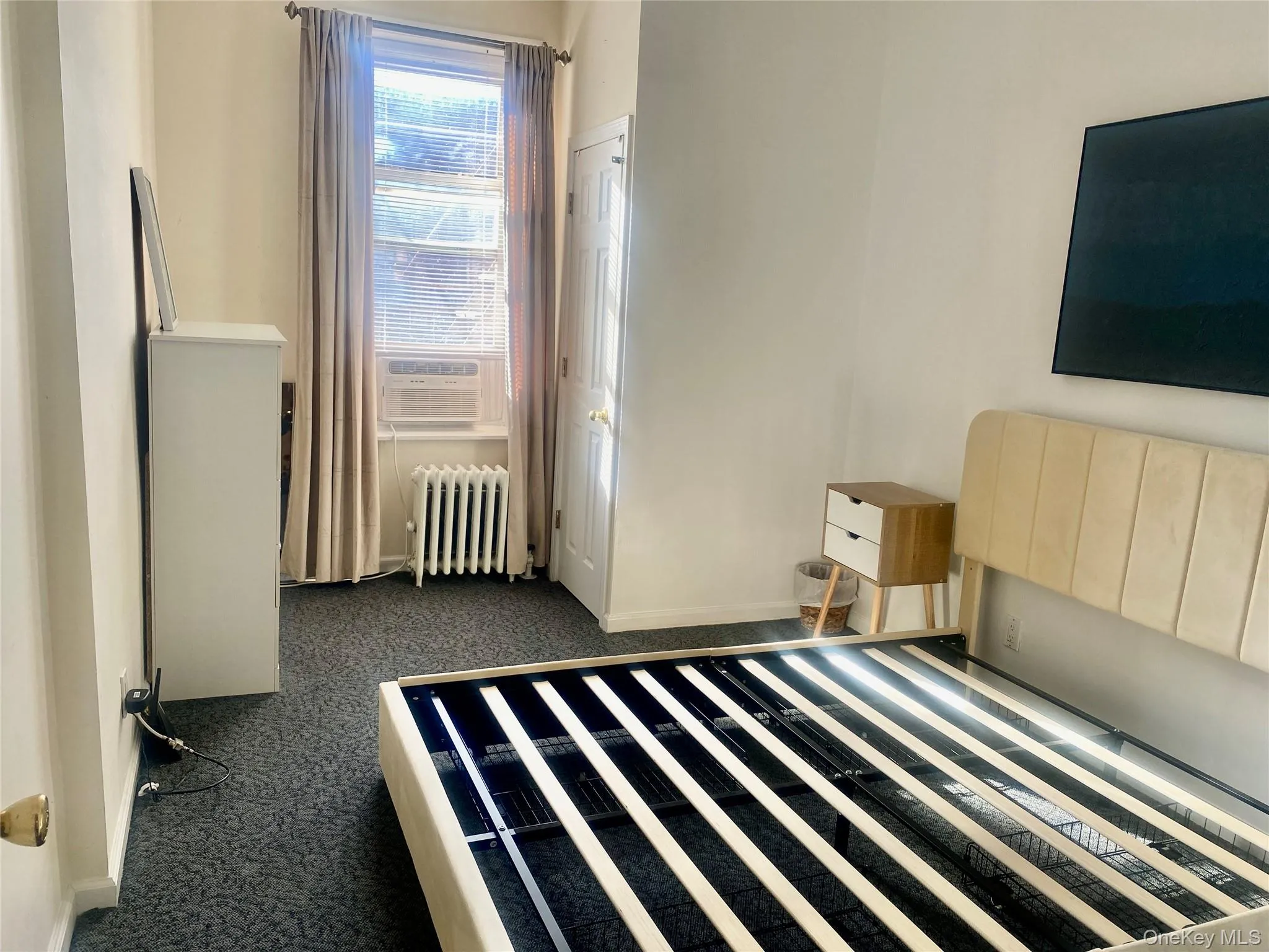 Bedroom with radiator, cooling unit, and dark colored carpet Bedroom with radiator, cooling unit, and dark colored carpet