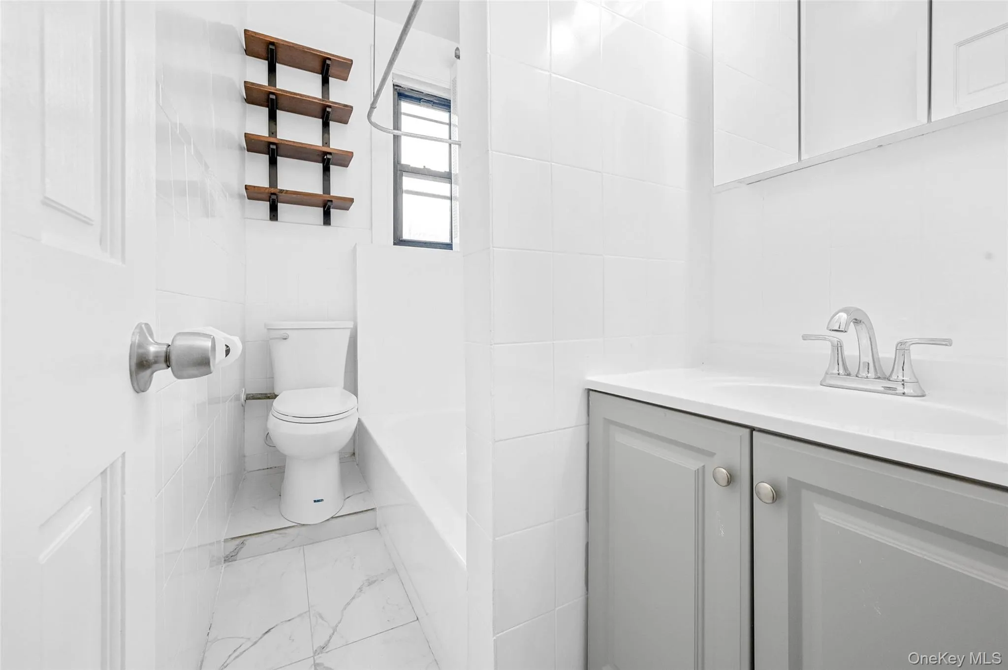Full bathroom with tile walls, vanity, marble look tile flooring, and shower / tub combination Full bathroom with tile walls, vanity, marble look tile flooring, and shower / tub combination