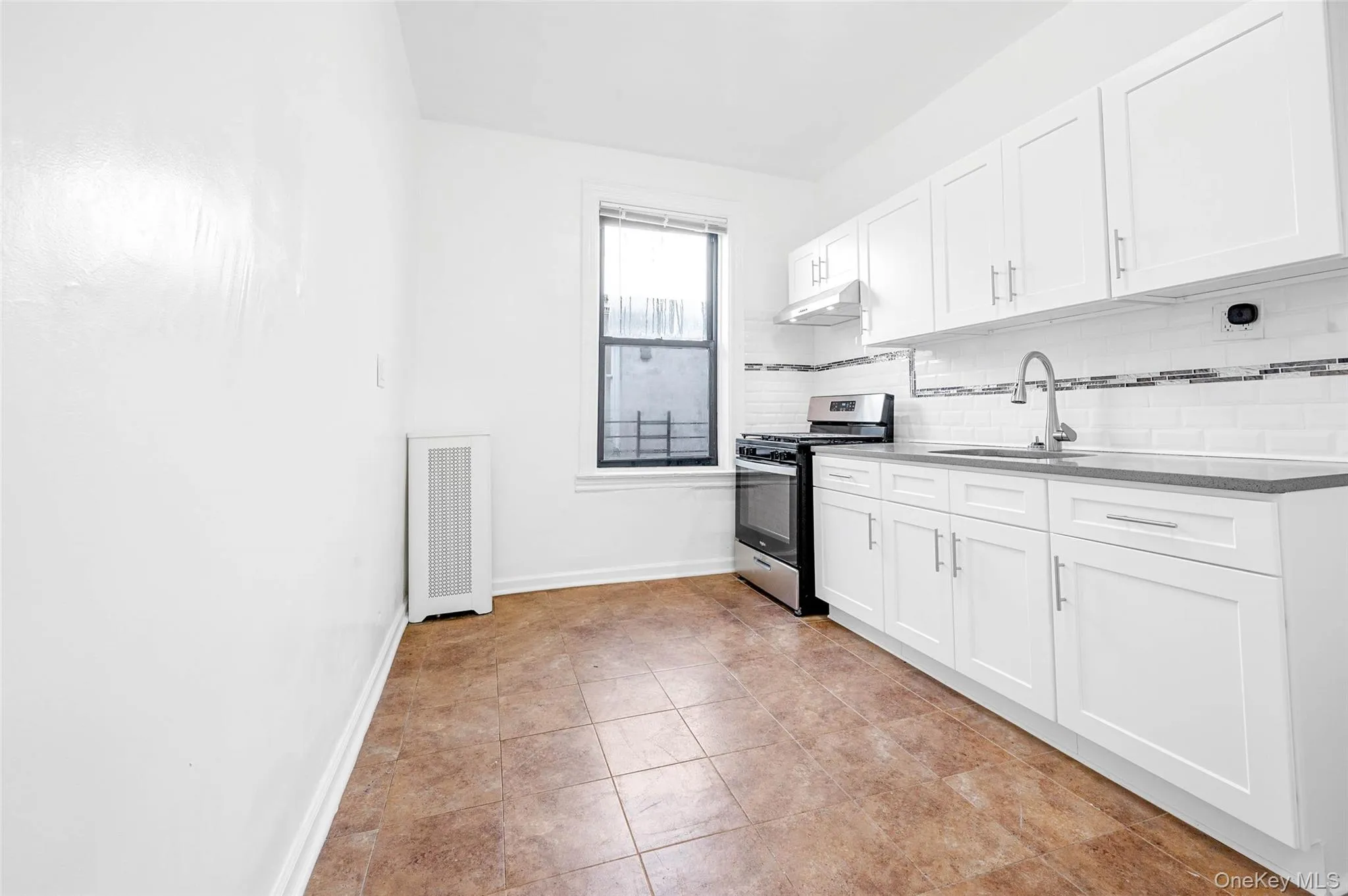 Kitchen with white cabinets, stainless steel range with gas cooktop, decorative backsplash, under cabinet range hood, and radiator heating unit Kitchen with white cabinets, stainless steel range with gas cooktop, decorative backsplash, under cabinet range hood, and radiator heating unit