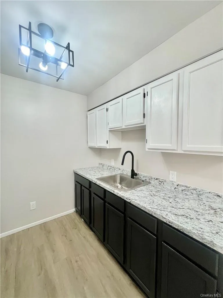 Kitchen with light hardwood / wood-style flooring, white cabinets, light stone countertops, sink, and a notable chandelier Kitchen with light hardwood / wood-style flooring, white cabinets, light stone countertops, sink, and a notable chandelier