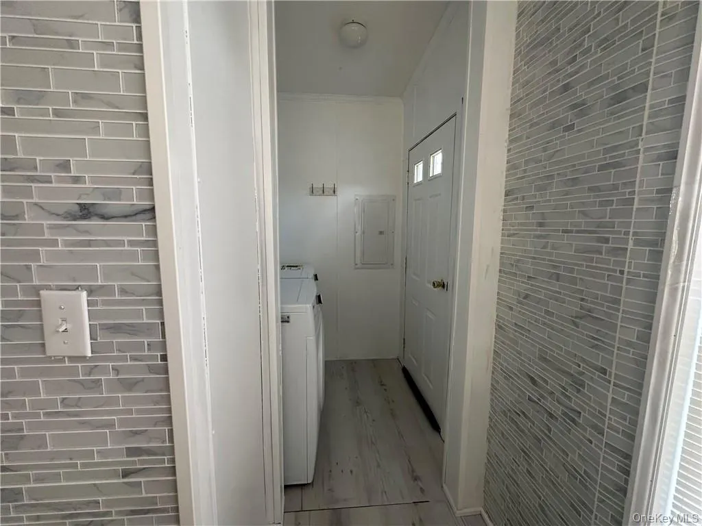 Hall featuring light wood-type flooring, washer / clothes dryer, and electric panel Hall featuring light wood-type flooring, washer / clothes dryer, and electric panel