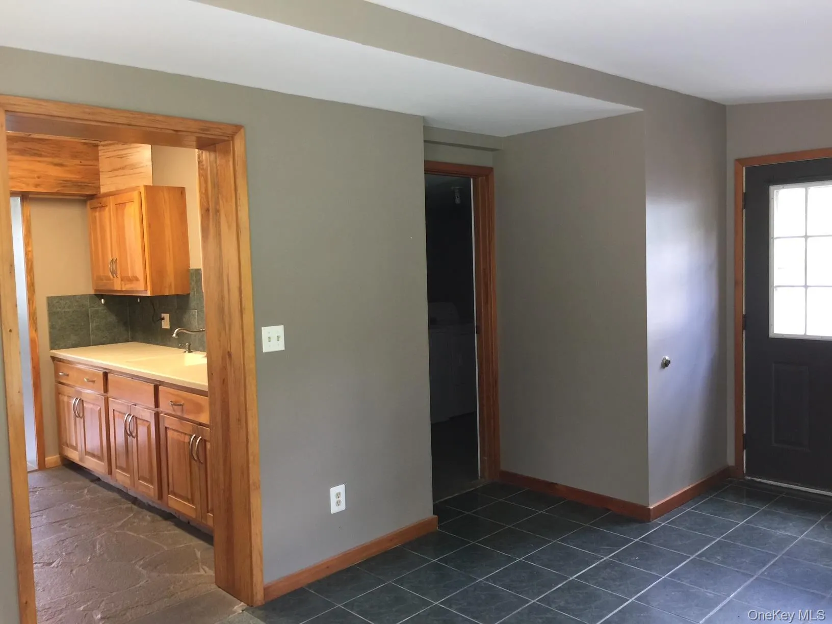 Kitchen featuring brown cabinetry, light countertops, decorative backsplash, and dark tile patterned flooring Kitchen featuring brown cabinetry, light countertops, decorative backsplash, and dark tile patterned flooring