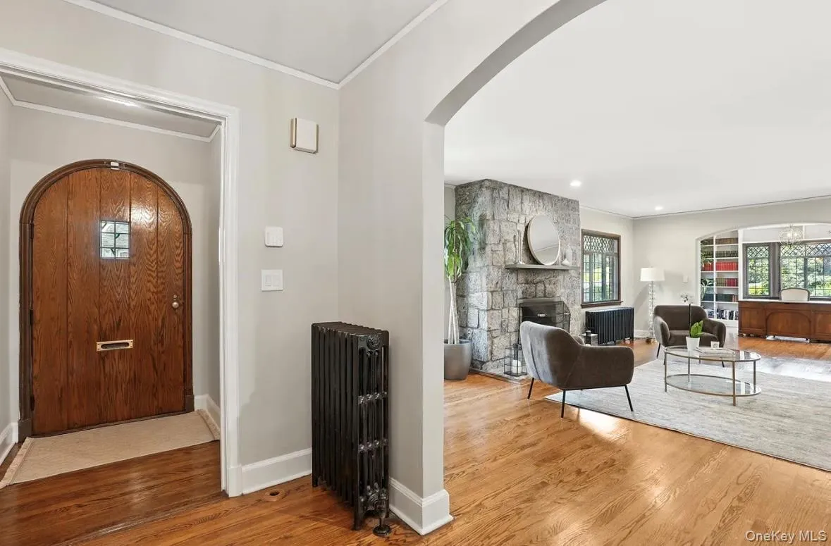 Entrance foyer featuring arched walkways, wood finished floors, radiator, ornamental molding, and a stone fireplace Entrance foyer featuring arched walkways, wood finished floors, radiator, ornamental molding, and a stone fireplace