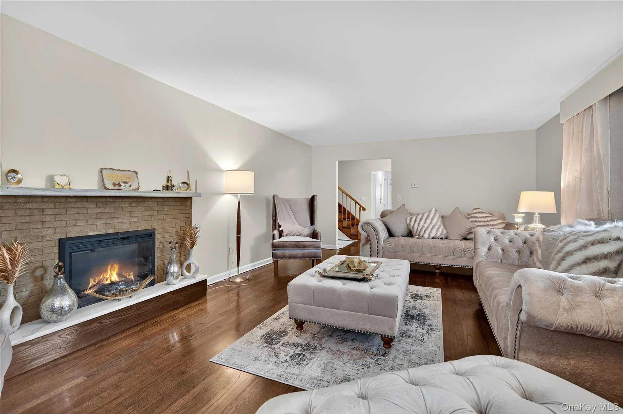 Living area featuring a brick fireplace, wood finished floors, and stairway Living area featuring a brick fireplace, wood finished floors, and stairway
