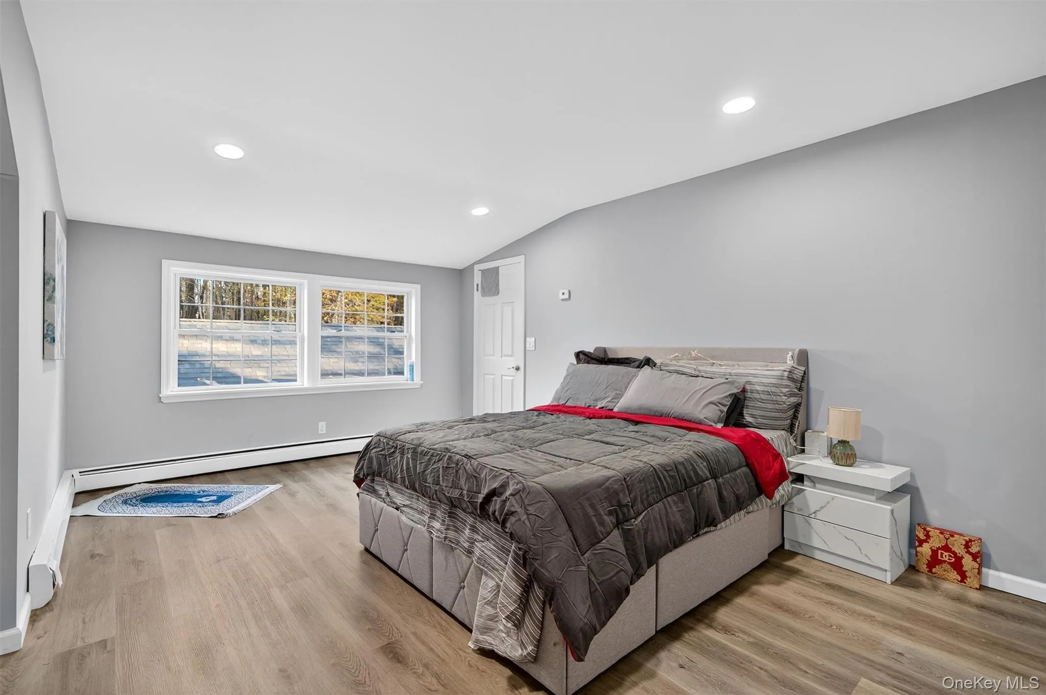 Bedroom with lofted ceiling, recessed lighting, a baseboard heating unit, and light wood-style floors Bedroom with lofted ceiling, recessed lighting, a baseboard heating unit, and light wood-style floors