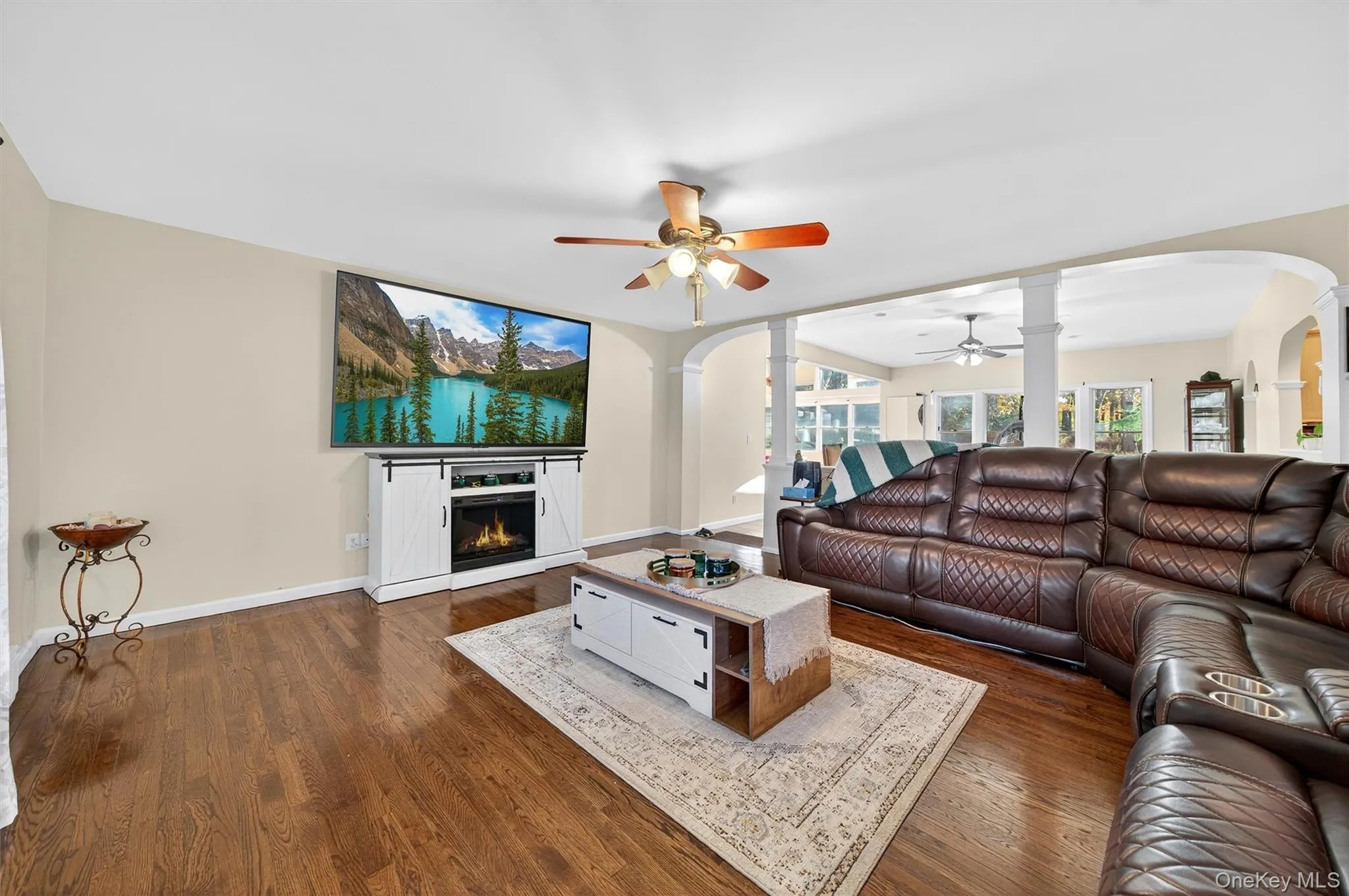 Living room featuring arched walkways, dark wood-style flooring, a lit fireplace, and ornate columns Living room featuring arched walkways, dark wood-style flooring, a lit fireplace, and ornate columns