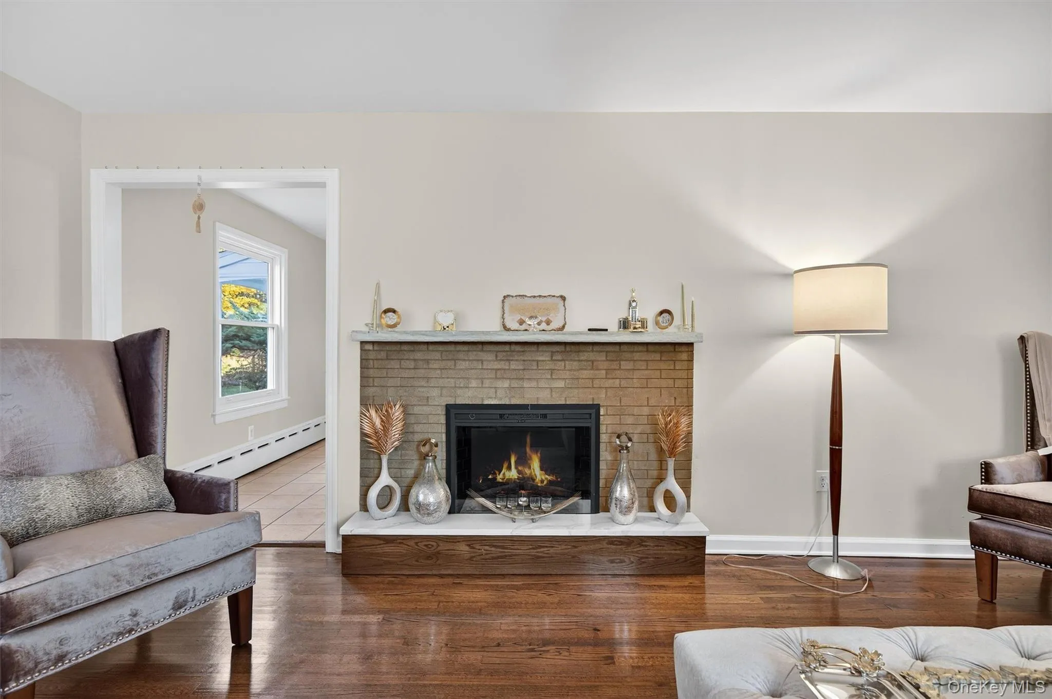 Living area with a brick fireplace, wood finished floors, and a baseboard radiator Living area with a brick fireplace, wood finished floors, and a baseboard radiator