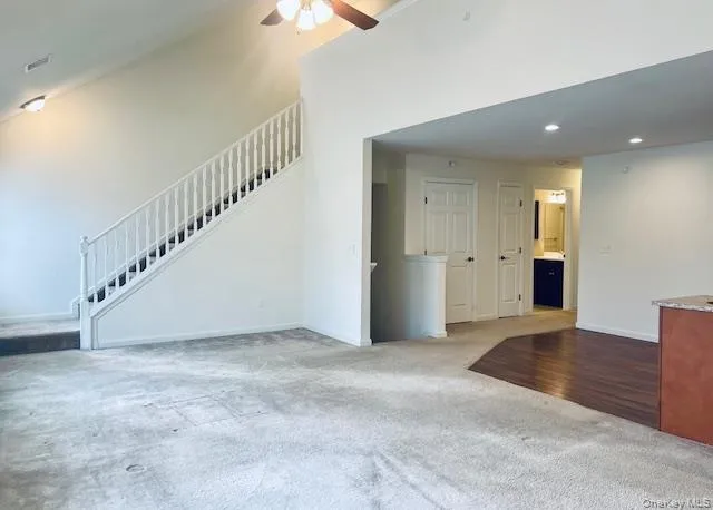 Unfurnished living room with light colored carpet, recessed lighting, ceiling fan, and stairway Unfurnished living room with light colored carpet, recessed lighting, ceiling fan, and stairway