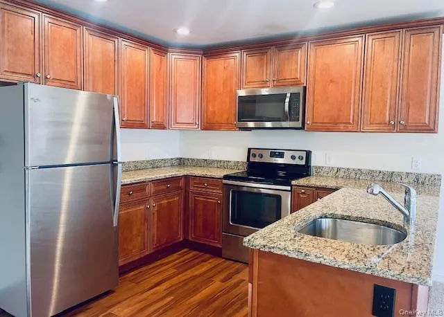 Kitchen with stainless steel appliances, light stone countertops, dark wood-style flooring, brown cabinets, and a peninsula Kitchen with stainless steel appliances, light stone countertops, dark wood-style flooring, brown cabinets, and a peninsula