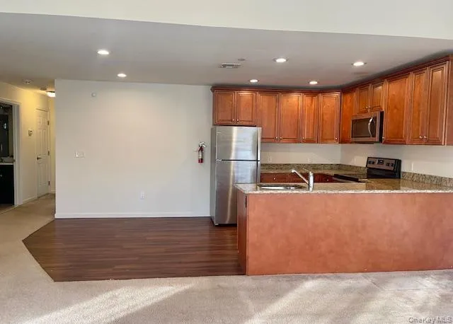 Kitchen featuring recessed lighting, light stone counters, open floor plan, brown cabinetry, and appliances with stainless steel finishes Kitchen featuring recessed lighting, light stone counters, open floor plan, brown cabinetry, and appliances with stainless steel finishes