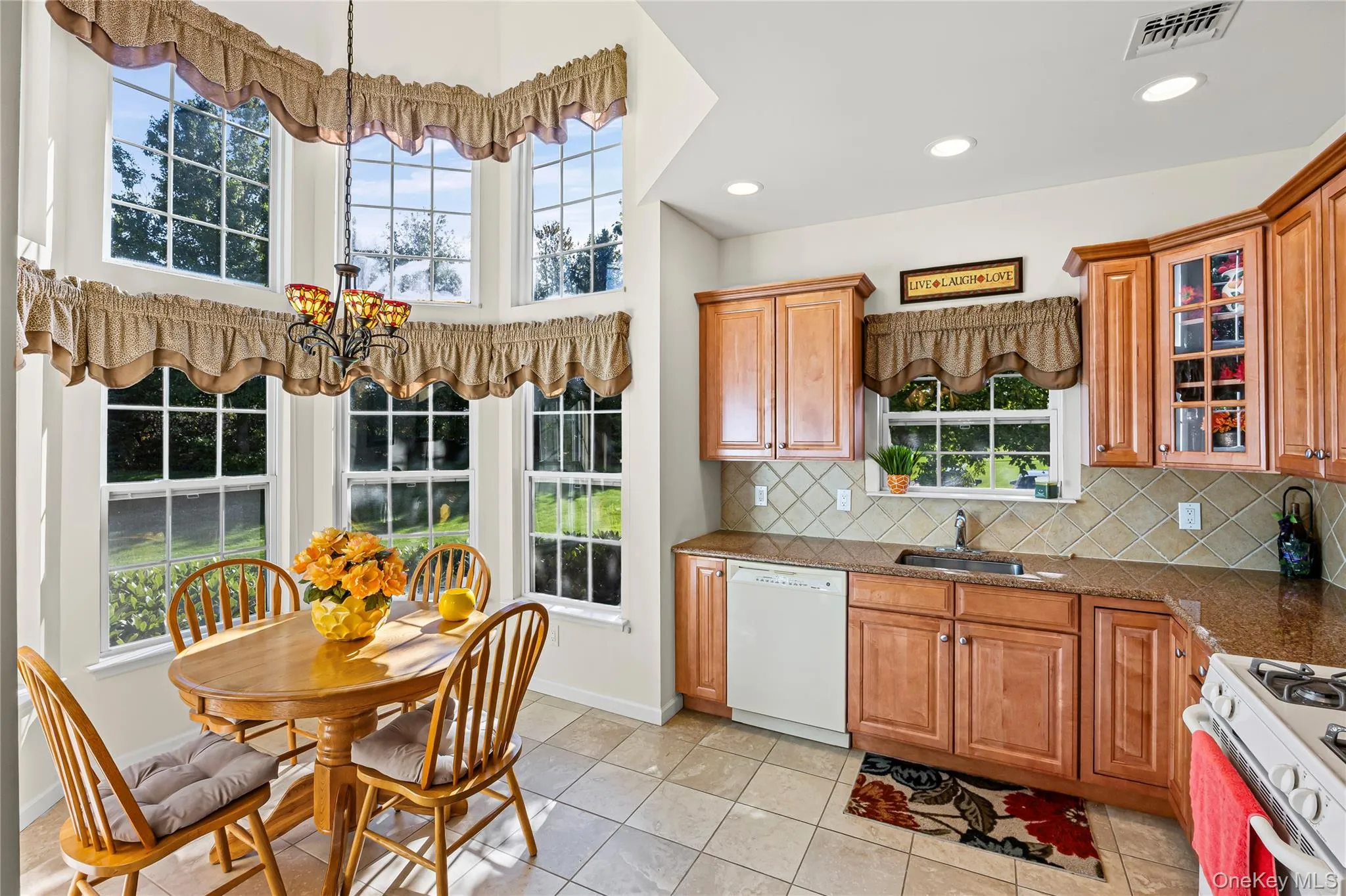 Kitchen featuring white appliances, brown cabinetry, glass insert cabinets, backsplash, and recessed lighting Kitchen featuring white appliances, brown cabinetry, glass insert cabinets, backsplash, and recessed lighting