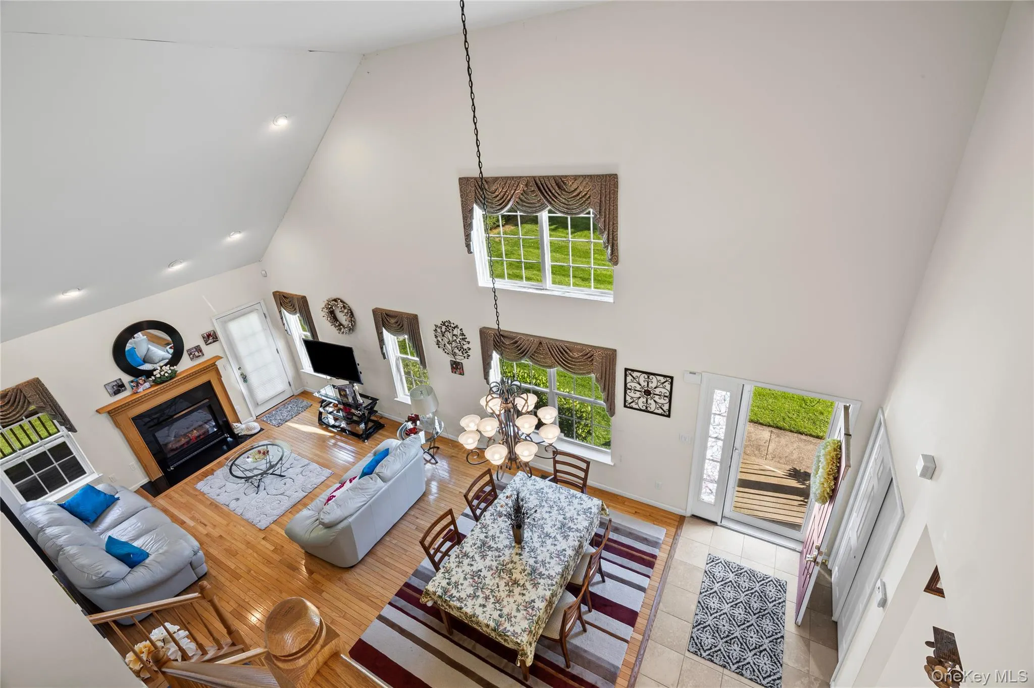 Living room with high vaulted ceiling, a fireplace with flush hearth, light wood-style flooring, and recessed lighting Living room with high vaulted ceiling, a fireplace with flush hearth, light wood-style flooring, and recessed lighting