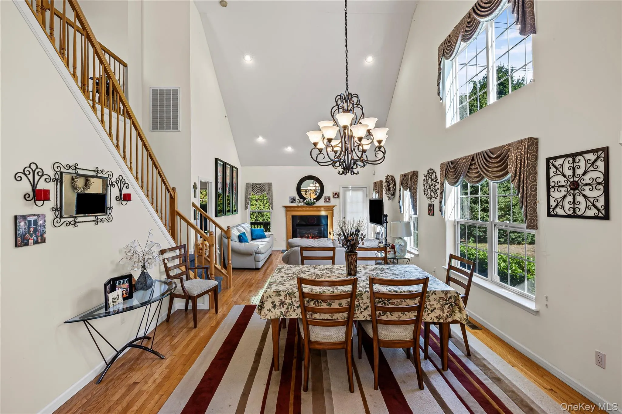Dining space with a high ceiling, a glass covered fireplace, recessed lighting, light wood-style flooring, and stairway Dining space with a high ceiling, a glass covered fireplace, recessed lighting, light wood-style flooring, and stairway
