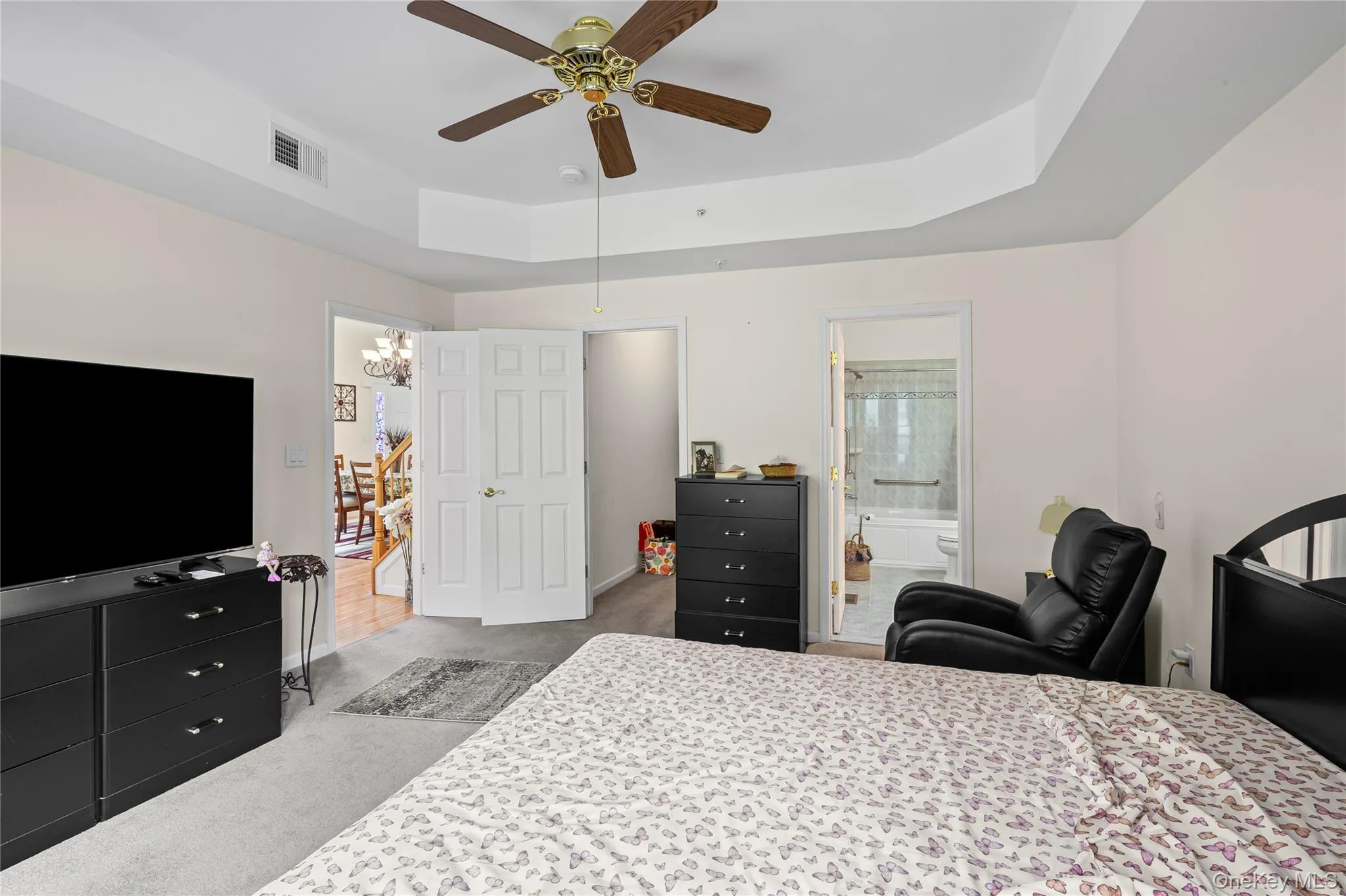 Carpeted bedroom featuring a tray ceiling, a chandelier, a ceiling fan, and ensuite bathroom Carpeted bedroom featuring a tray ceiling, a chandelier, a ceiling fan, and ensuite bathroom