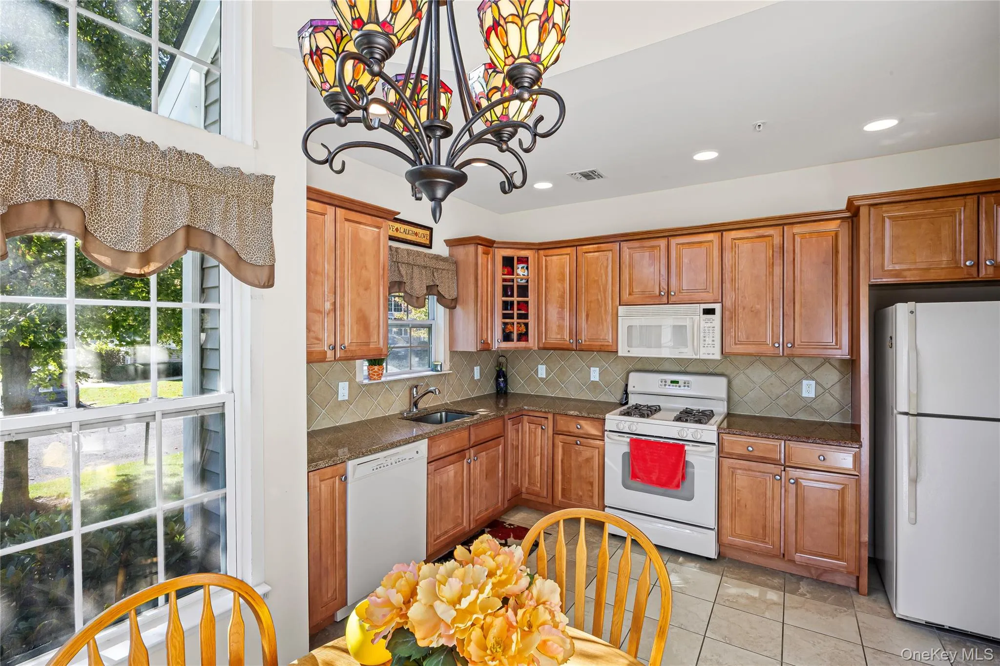 Kitchen with white appliances, tasteful backsplash, glass insert cabinets, brown cabinets, and recessed lighting Kitchen with white appliances, tasteful backsplash, glass insert cabinets, brown cabinets, and recessed lighting