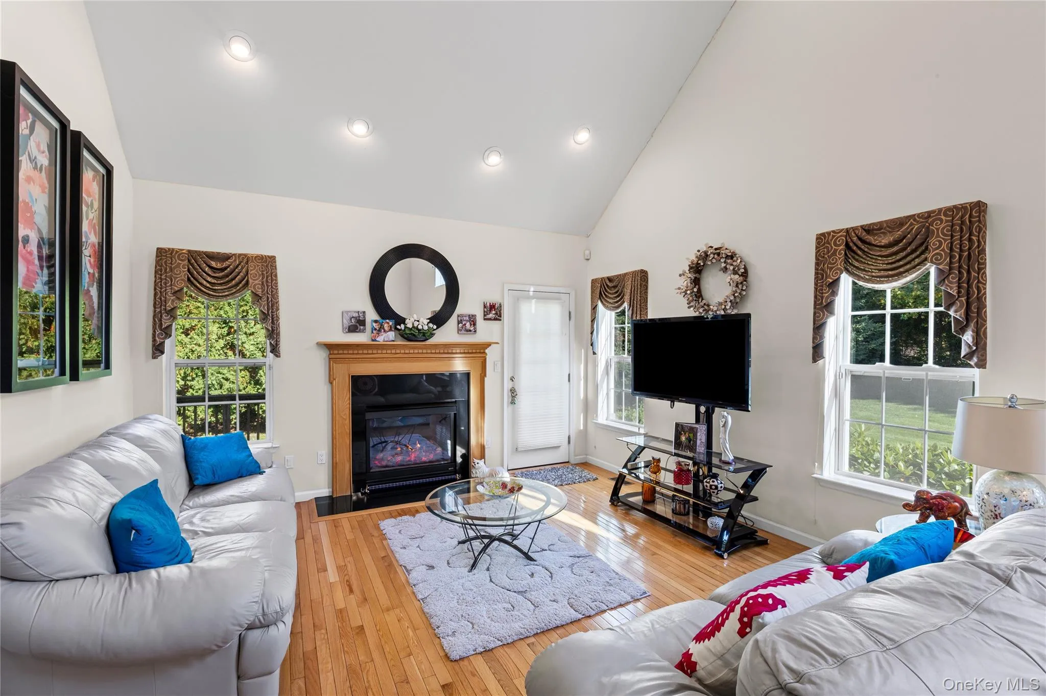 Living room featuring high vaulted ceiling, hardwood / wood-style flooring, a fireplace with flush hearth, and recessed lighting Living room featuring high vaulted ceiling, hardwood / wood-style flooring, a fireplace with flush hearth, and recessed lighting