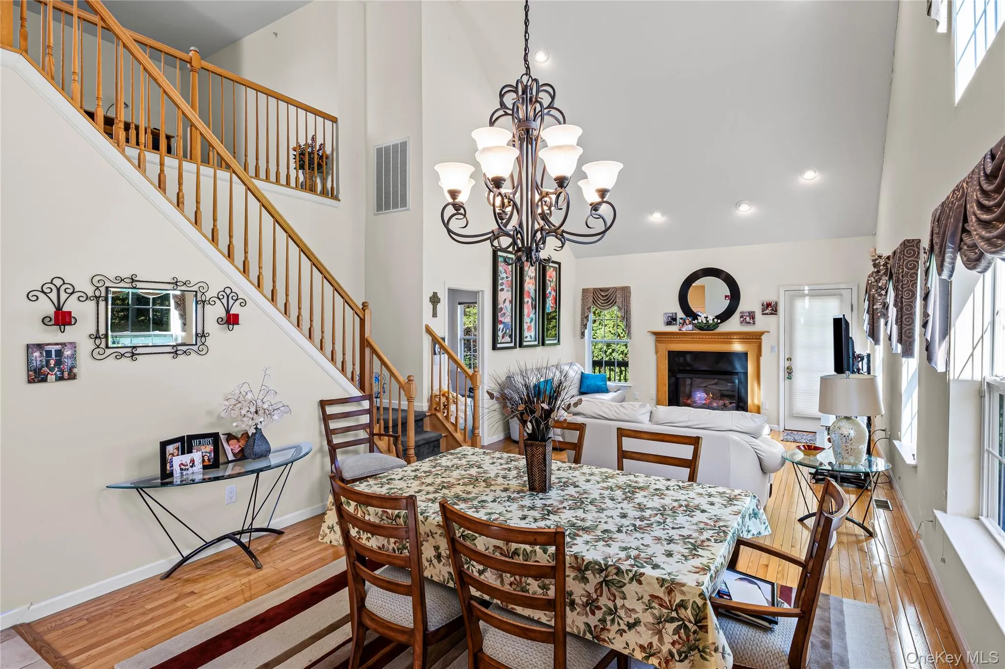 Dining room with a towering ceiling, a glass covered fireplace, stairs, light wood finished floors, and recessed lighting Dining room with a towering ceiling, a glass covered fireplace, stairs, light wood finished floors, and recessed lighting