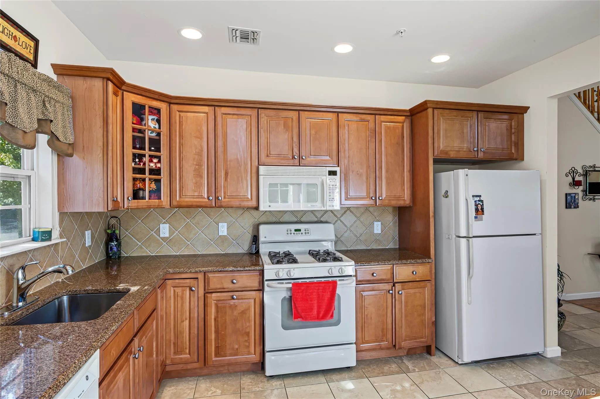 Kitchen featuring white appliances, brown cabinetry, dark stone countertops, tasteful backsplash, and recessed lighting Kitchen featuring white appliances, brown cabinetry, dark stone countertops, tasteful backsplash, and recessed lighting