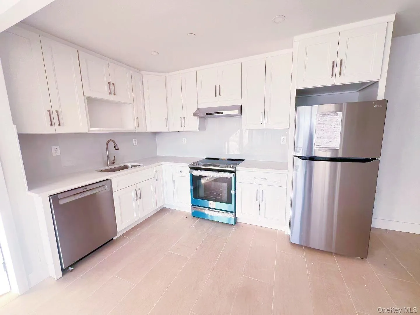 Kitchen with appliances with stainless steel finishes, white cabinetry, under cabinet range hood, open shelves, and recessed lighting Kitchen with appliances with stainless steel finishes, white cabinetry, under cabinet range hood, open shelves, and recessed lighting