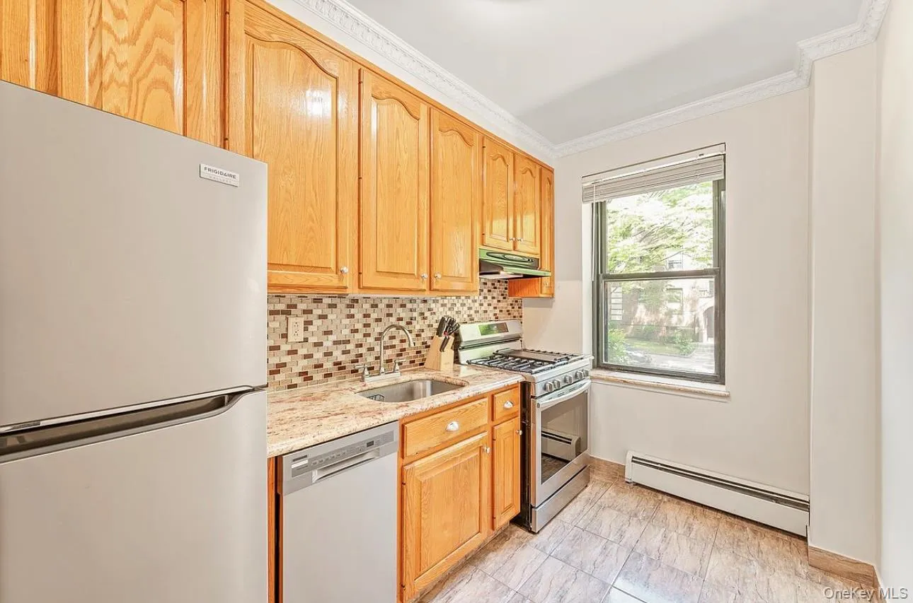 Kitchen with appliances with stainless steel finishes, baseboard heating, light stone counters, decorative backsplash, and crown molding Kitchen with appliances with stainless steel finishes, baseboard heating, light stone counters, decorative backsplash, and crown molding