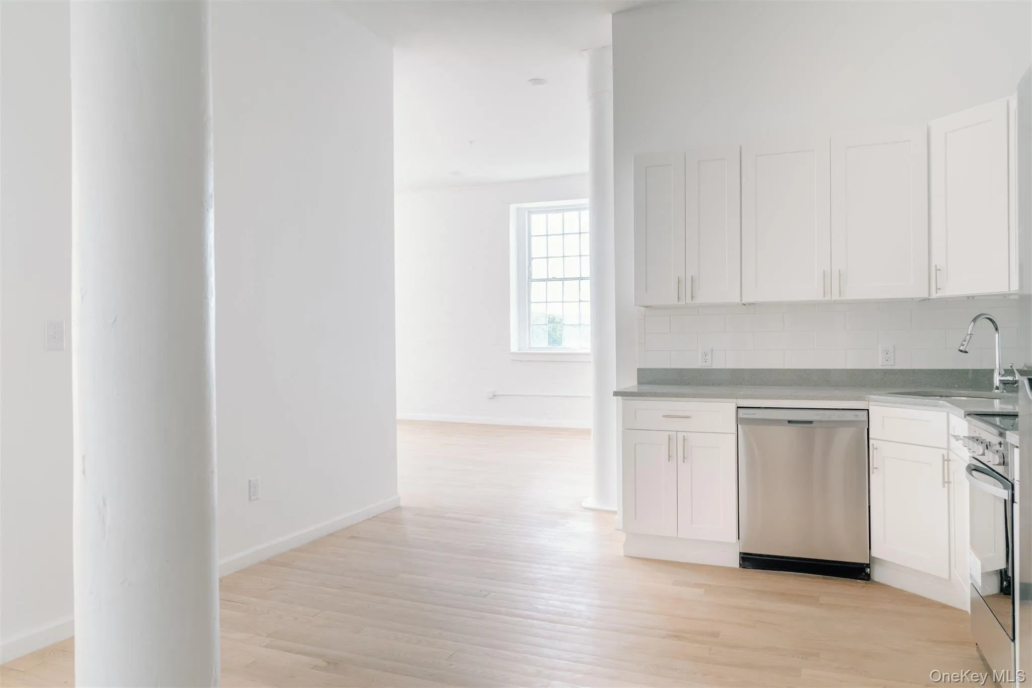 Kitchen with white cabinets, appliances with stainless steel finishes, backsplash, light stone countertops, and light wood-style flooring Kitchen with white cabinets, appliances with stainless steel finishes, backsplash, light stone countertops, and light wood-style flooring