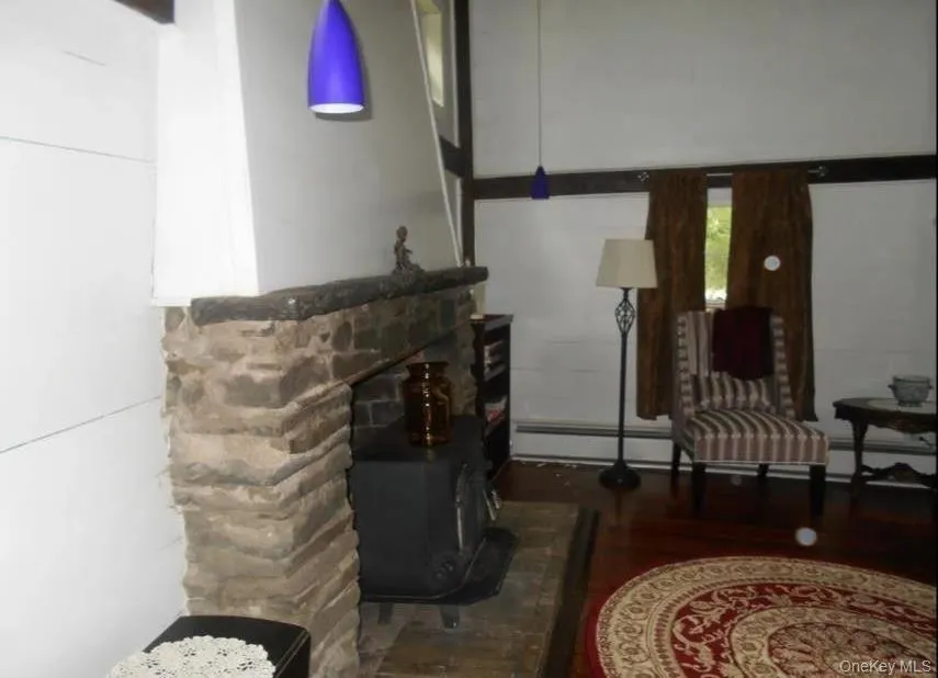 Living area with a wood stove, dark wood-style flooring, a baseboard heating unit, and baseboard heating Living area with a wood stove, dark wood-style flooring, a baseboard heating unit, and baseboard heating