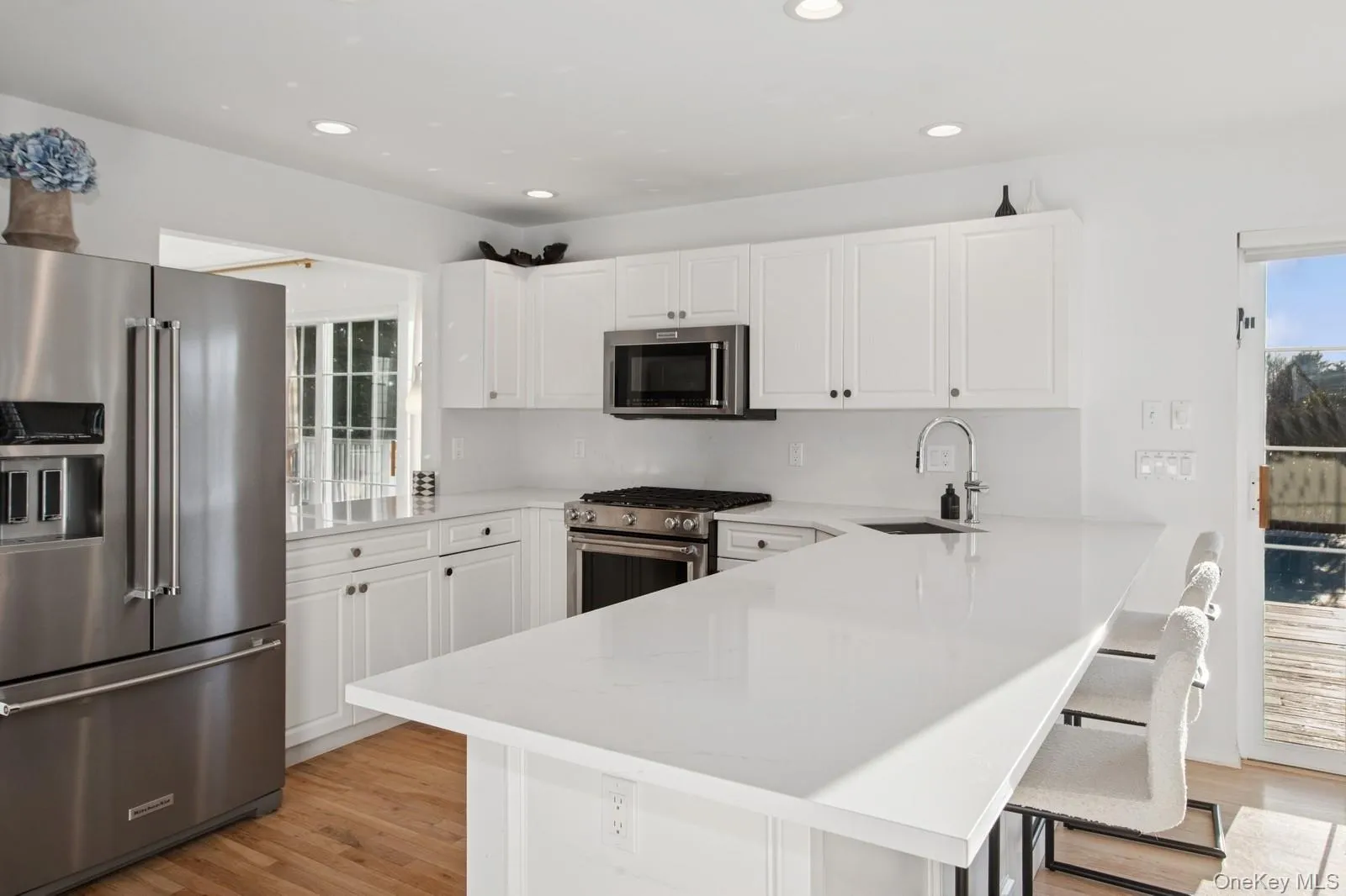 Kitchen with stainless steel appliances, white cabinets, light wood-style flooring, a breakfast bar, and recessed lighting Kitchen with stainless steel appliances, white cabinets, light wood-style flooring, a breakfast bar, and recessed lighting