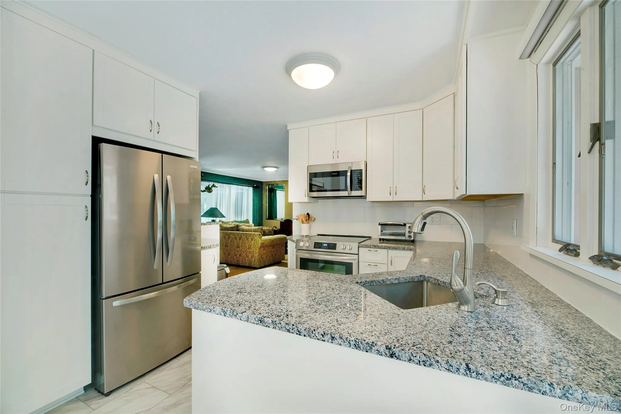 Kitchen featuring light stone counters, stainless steel appliances, a peninsula, and white cabinets Kitchen featuring light stone counters, stainless steel appliances, a peninsula, and white cabinets