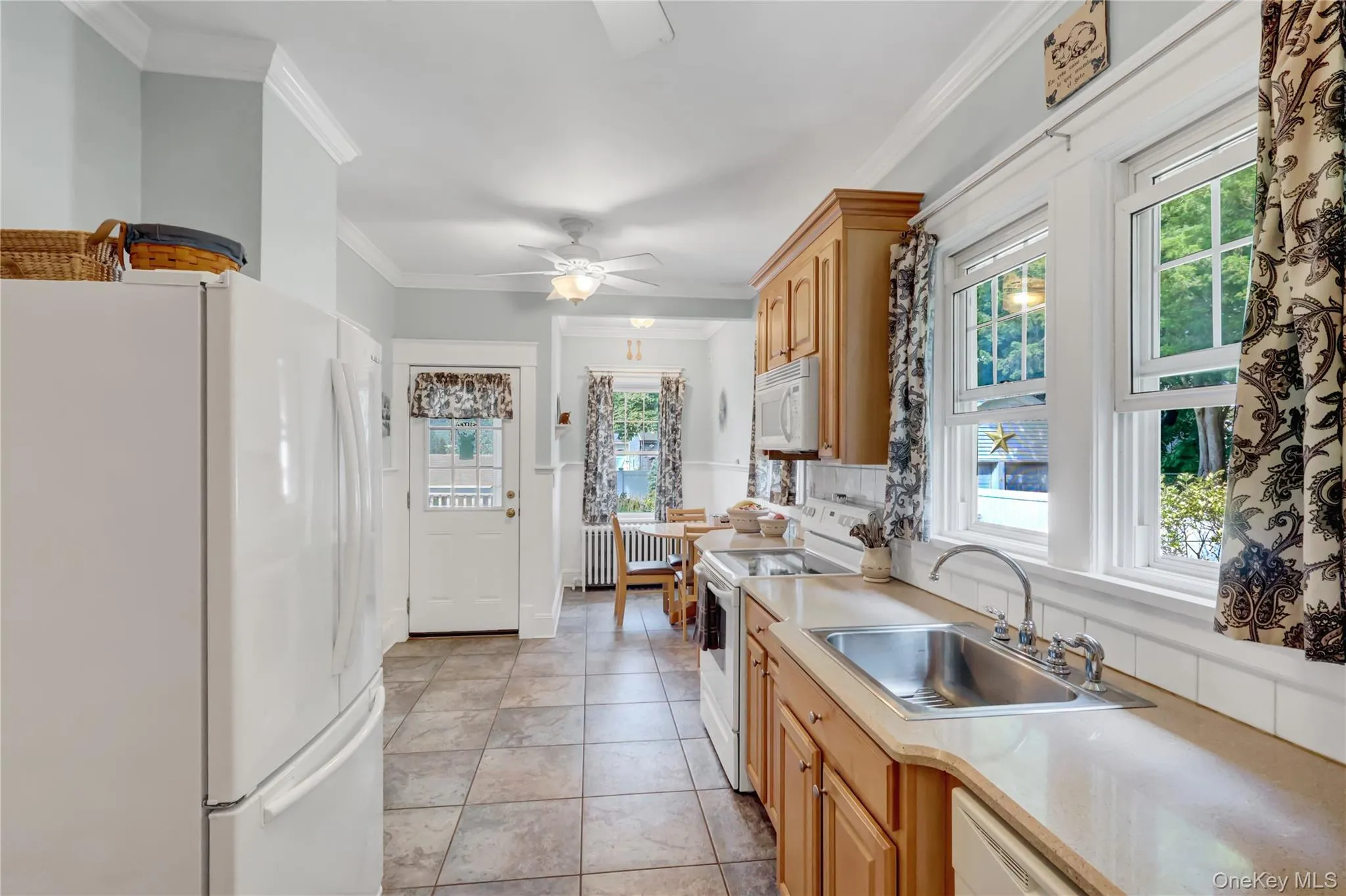 Kitchen featuring tile flooring, light wood cabinetry, white appliances, and a double-basin stainless steel sink Kitchen featuring tile flooring, light wood cabinetry, white appliances, and a double-basin stainless steel sink