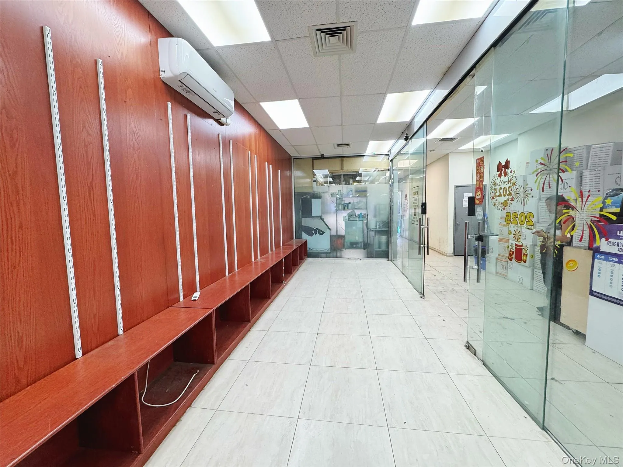 Hallway with a paneled ceiling, light tile patterned flooring, and a wall mounted air conditioner Hallway with a paneled ceiling, light tile patterned flooring, and a wall mounted air conditioner