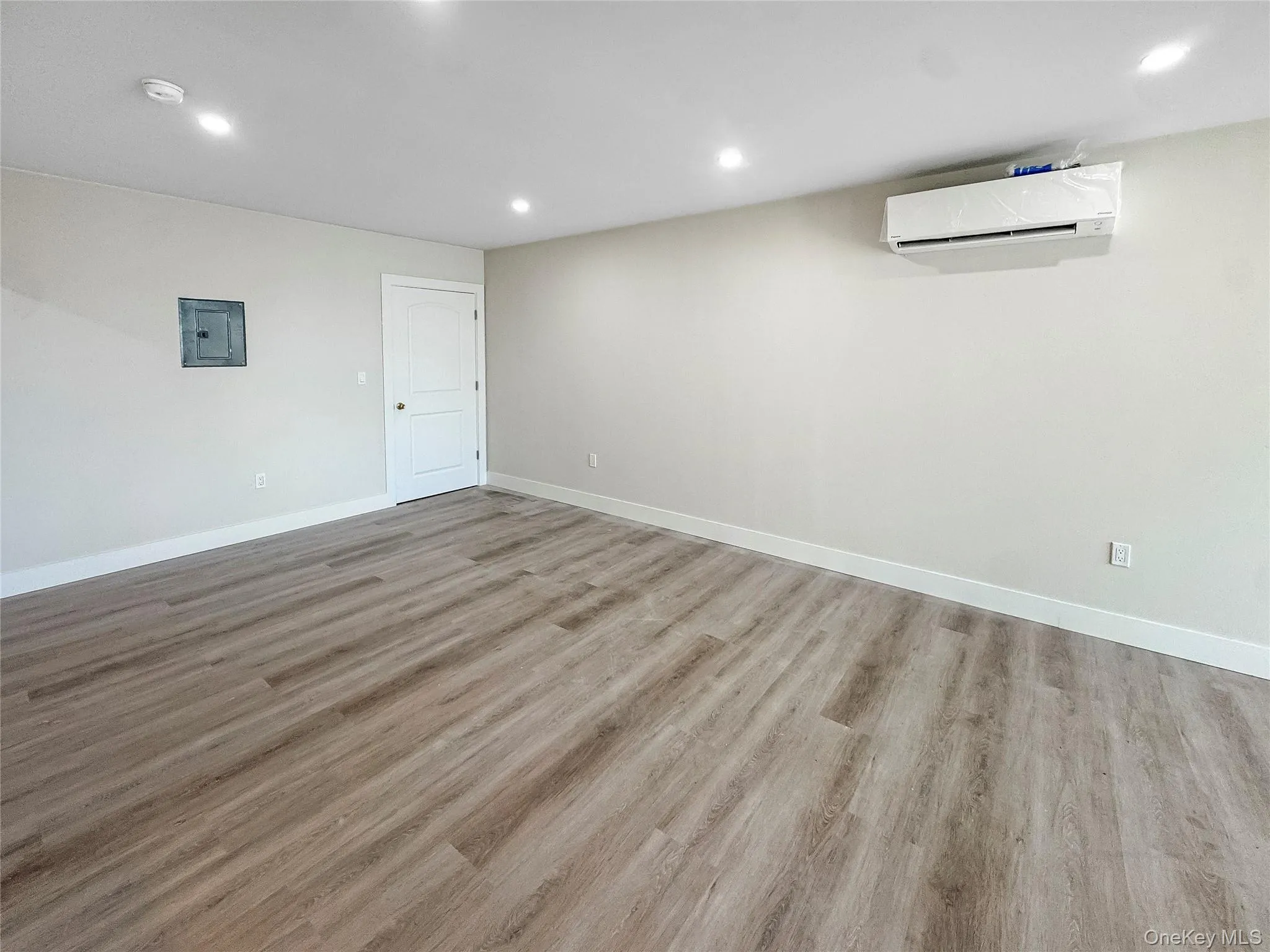 Below grade area featuring recessed lighting, light wood-style floors, electric panel, and a wall mounted air conditioner Below grade area featuring recessed lighting, light wood-style floors, electric panel, and a wall mounted air conditioner