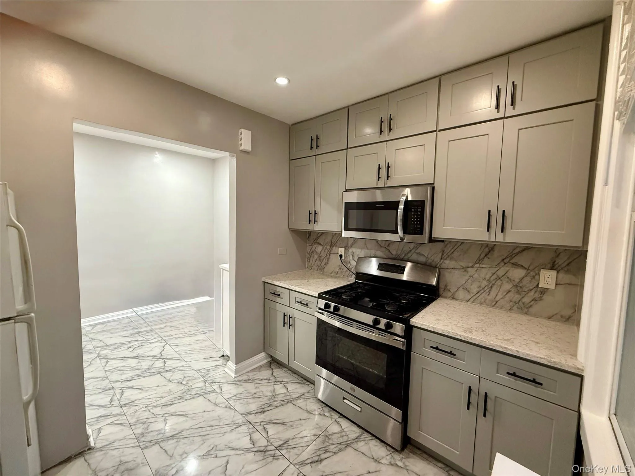 Kitchen featuring gray cabinetry, appliances with stainless steel finishes, light stone counters, light marble finish floors, and decorative backsplash Kitchen featuring gray cabinetry, appliances with stainless steel finishes, light stone counters, light marble finish floors, and decorative backsplash